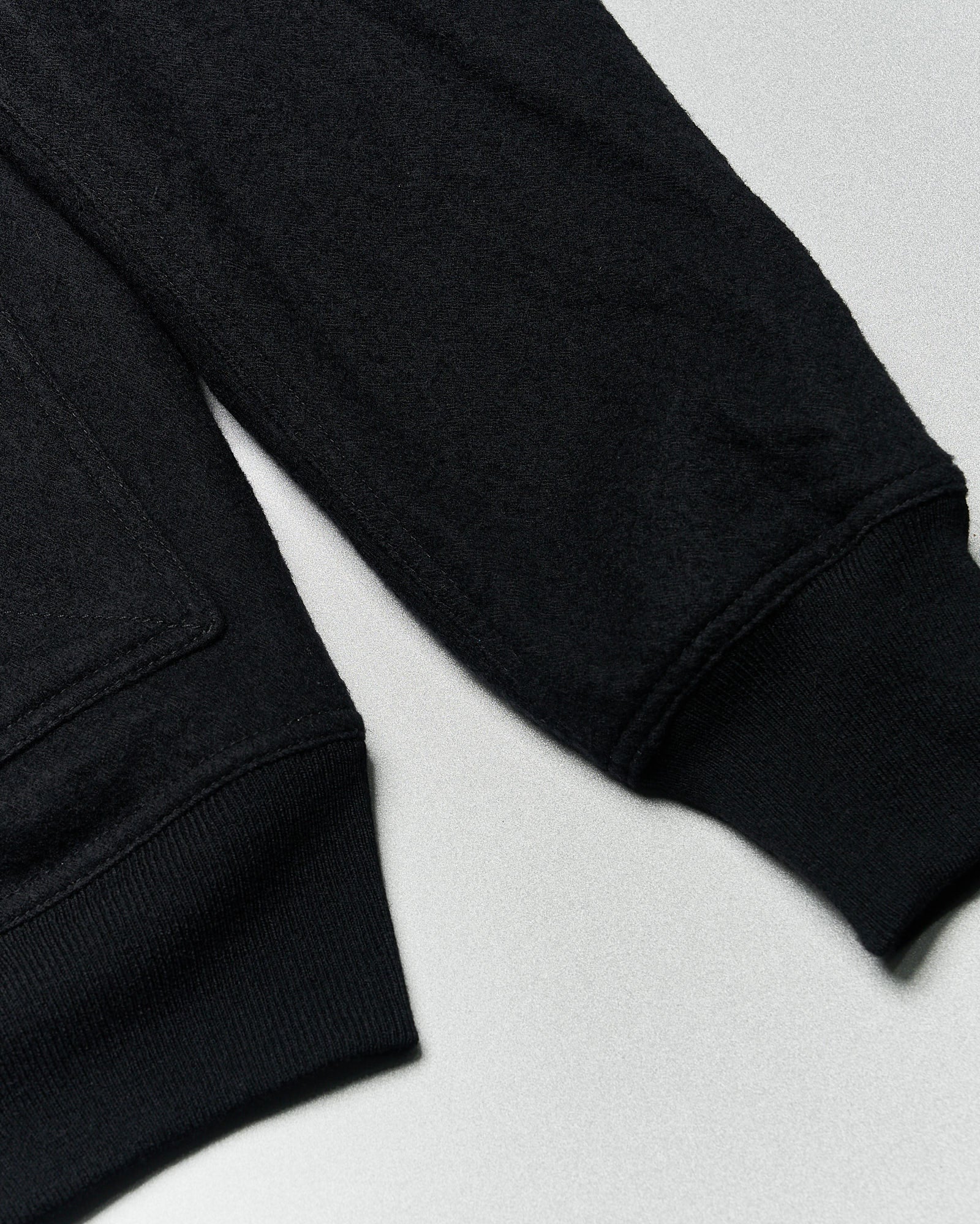 Close-up of a black Rick Owens bomber jacket with visible sleeves and cuffs, laying flat on a light gray surface. 