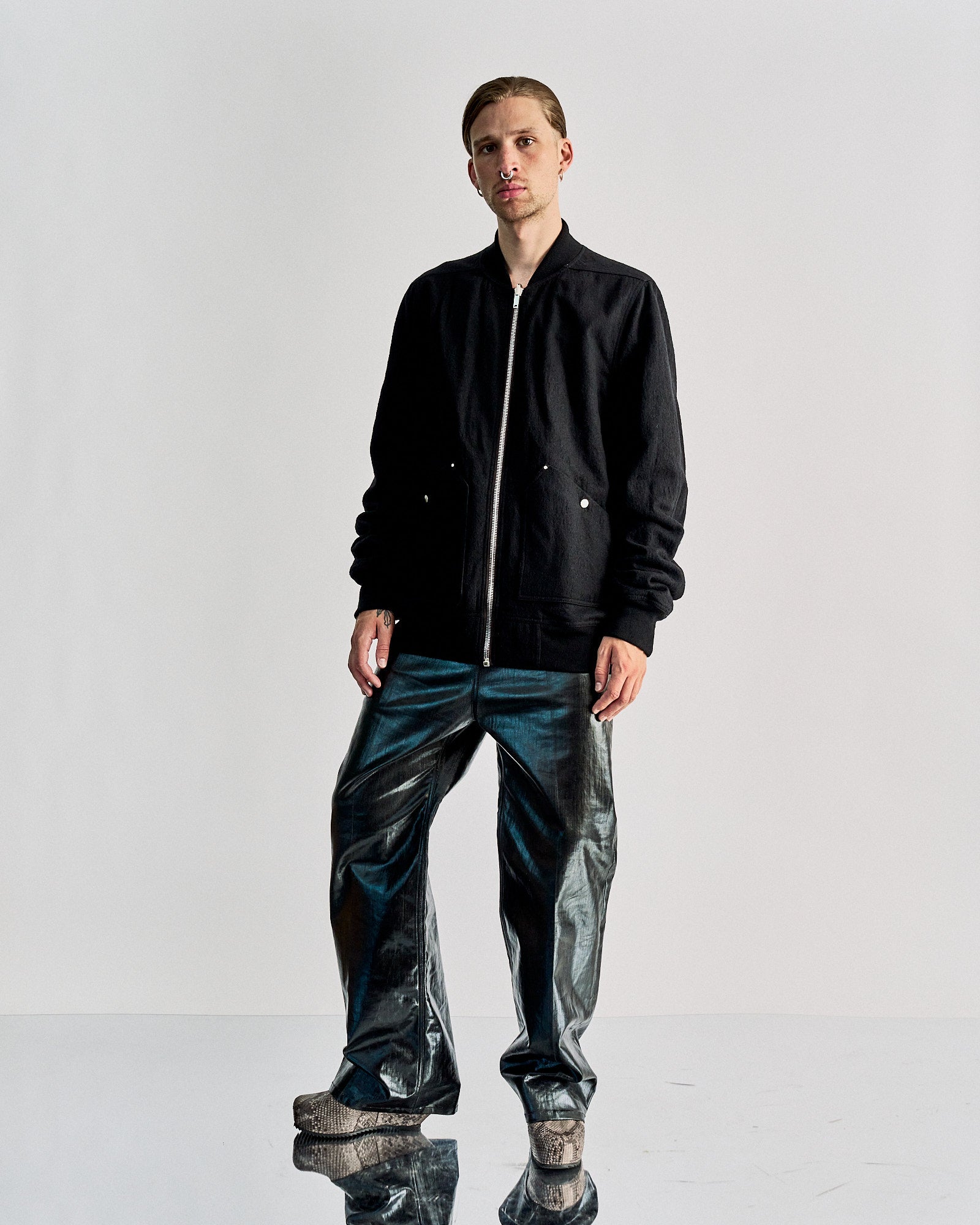 Person wearing a black zip-up Rick Owens jacket with silver buttons, paired with metallic pants. They stand against a plain light gray background.