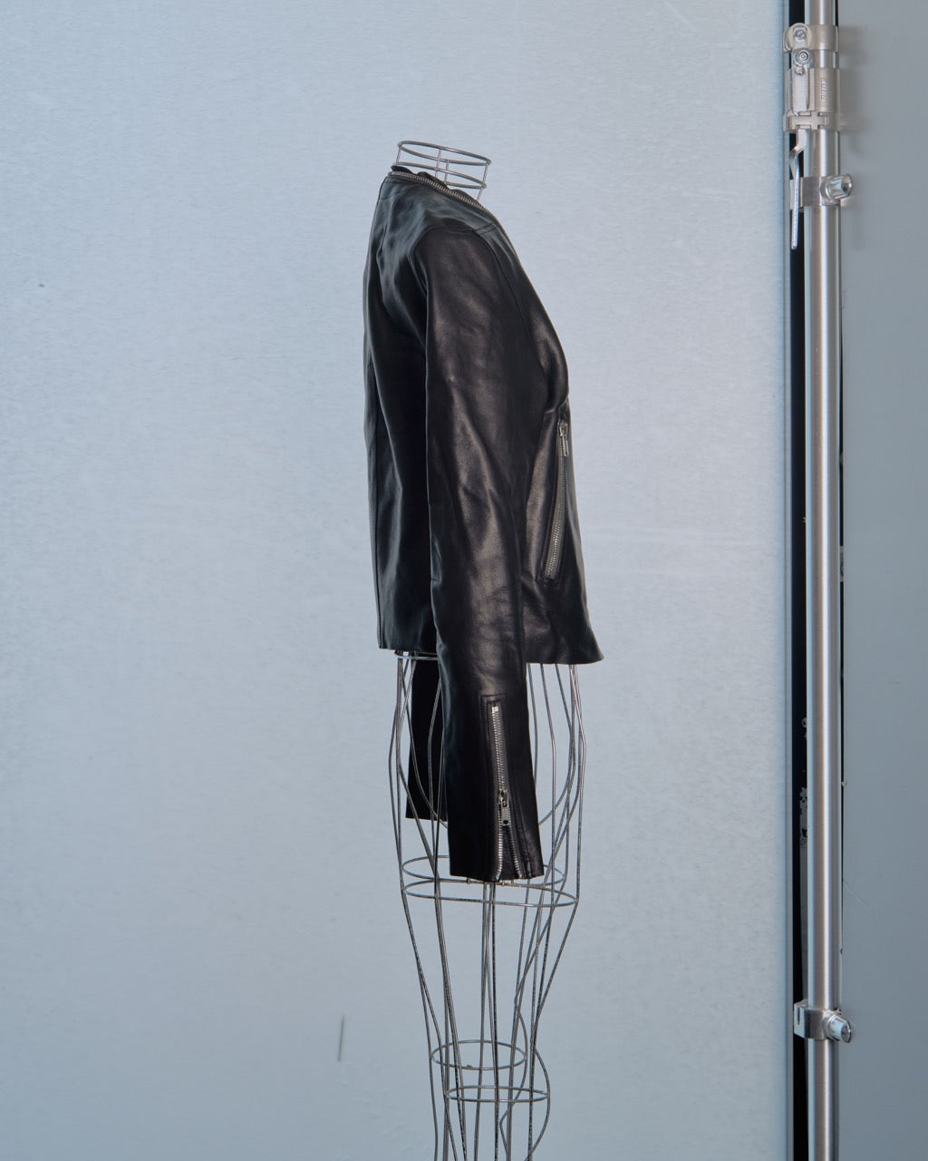 Black leather Rick Owens jacket on a wire mannequin against a light blue wall.