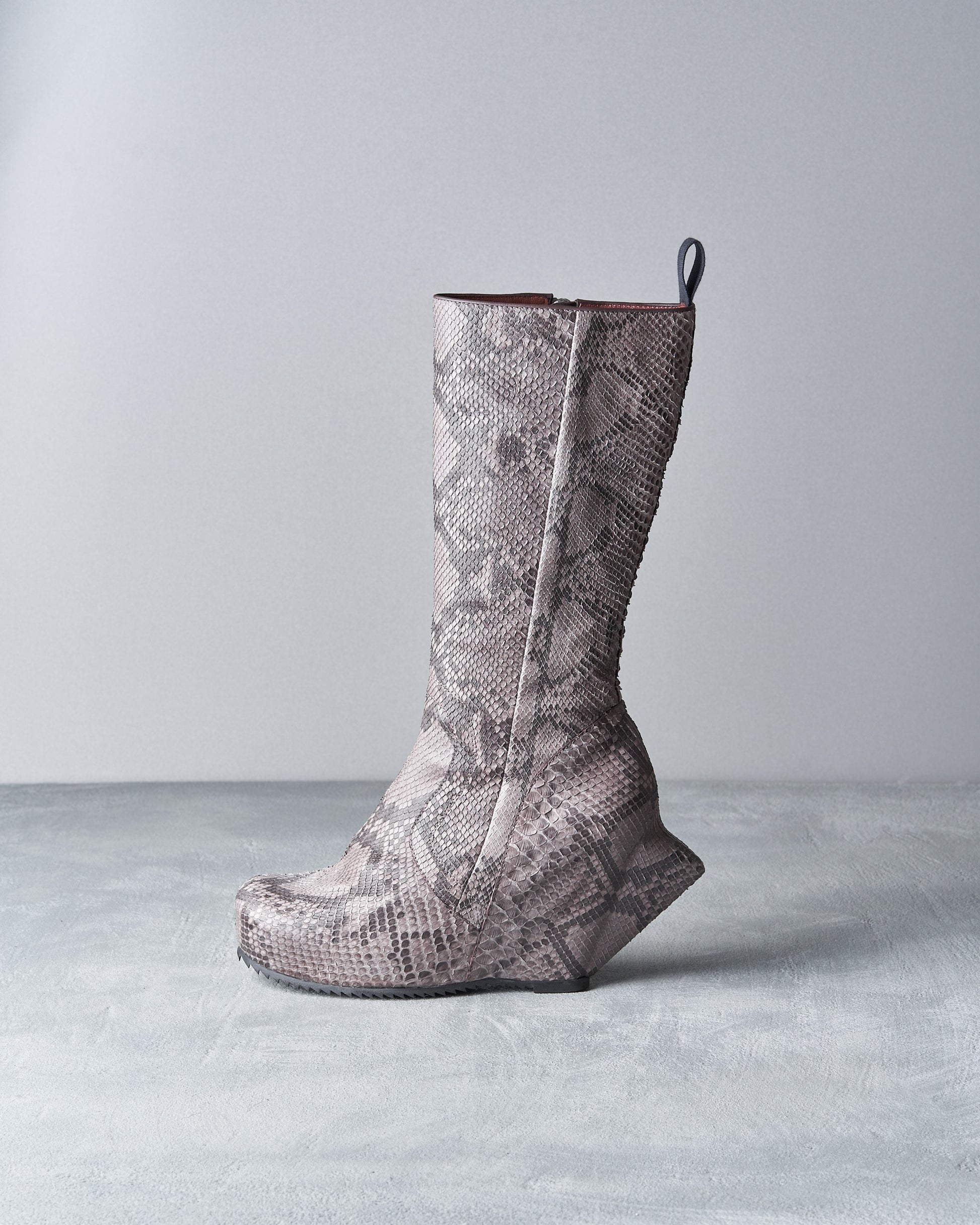 A high-heeled Rick Owens boot with a patterned snakeskin texture and geometric wedge heel, set against a minimalist grey background.