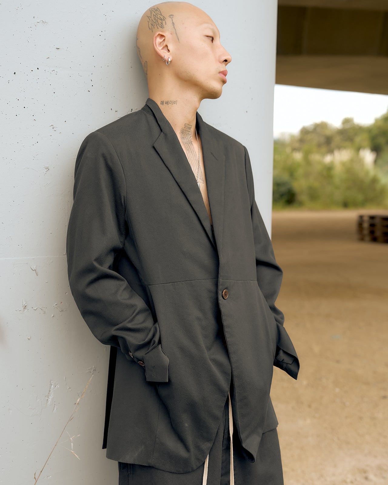 A person wearing a long, slim Rick Owens blazer with a minimalist design, featuring a half-collar and grid panelled construction.