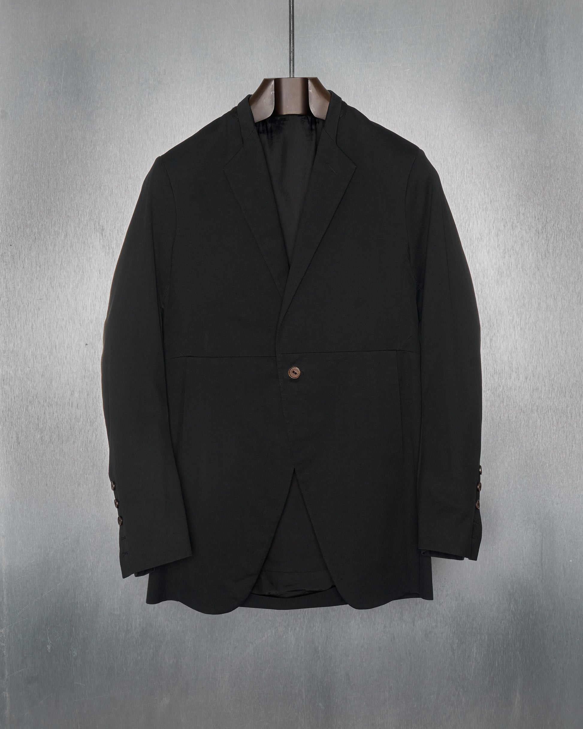 A black Rick Owens blazer with a minimalist half-collar, grid panelled construction, and a leather single-button closure. The jacket is displayed against a textured grey background.