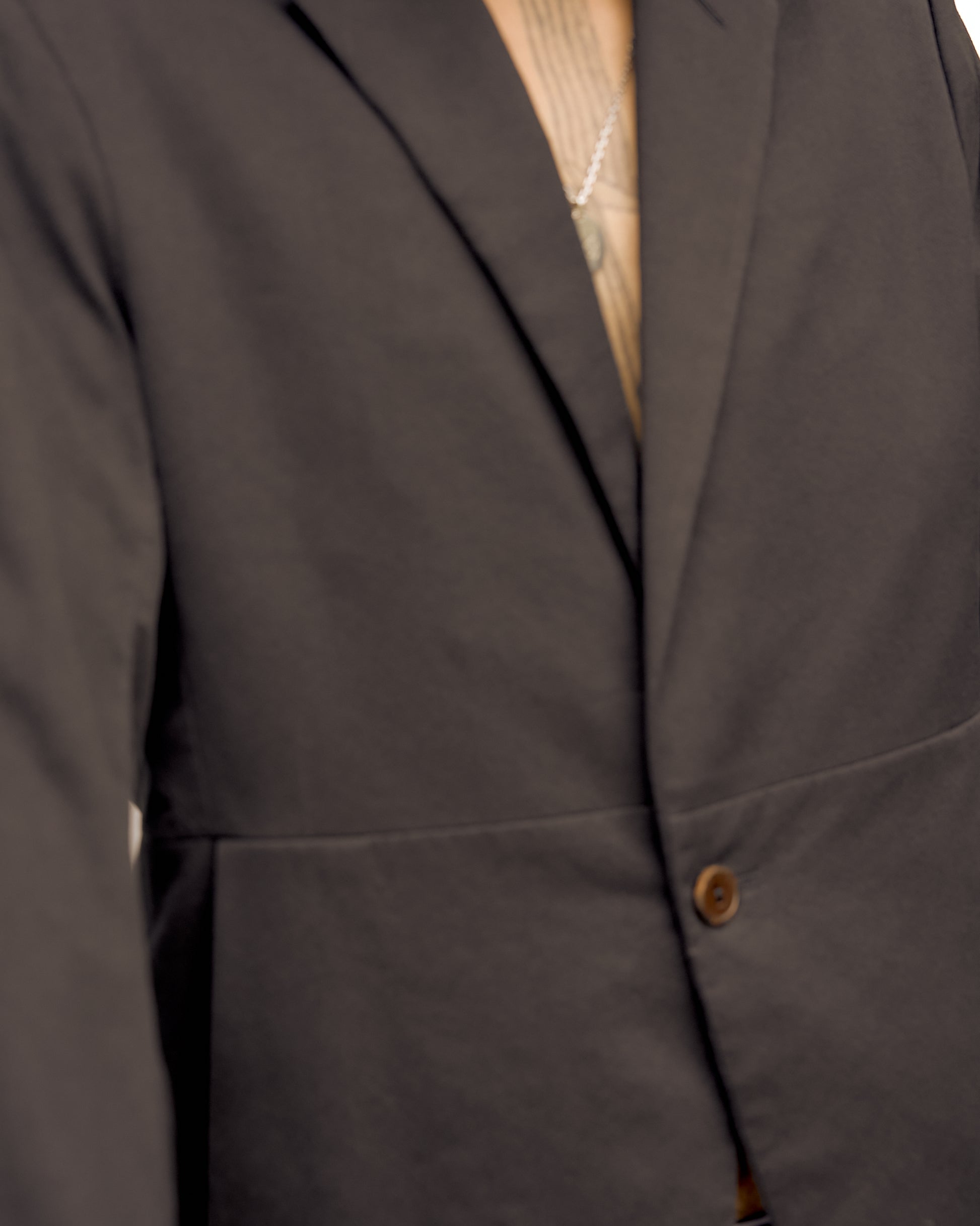 Close-up of a person wearing a dark Rick Owens blazer over a light shirt with a visible necklace chain, conveying a formal and elegant style.