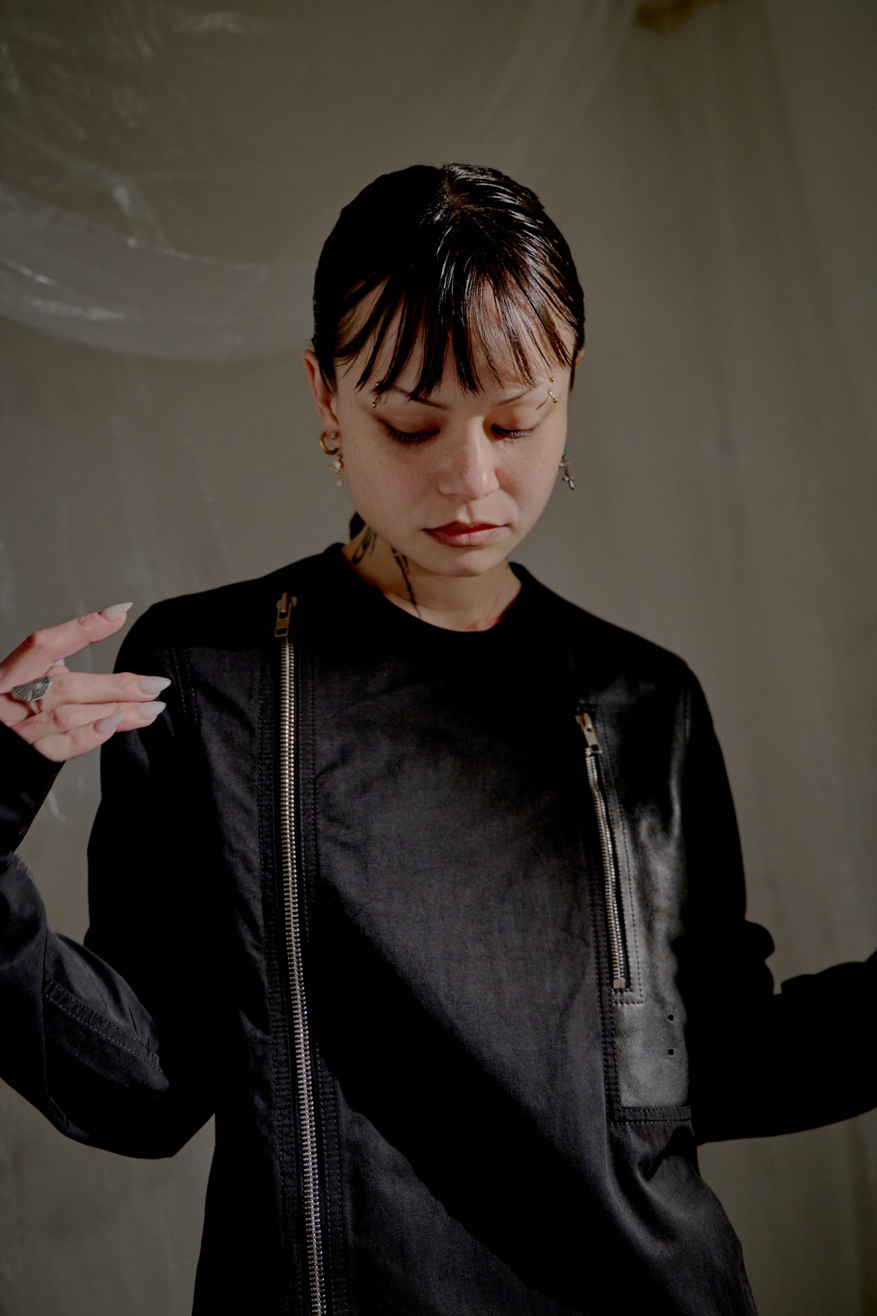 Person wearing a dark Rick Owens coat and boots standing in a room with white fabric draped around.