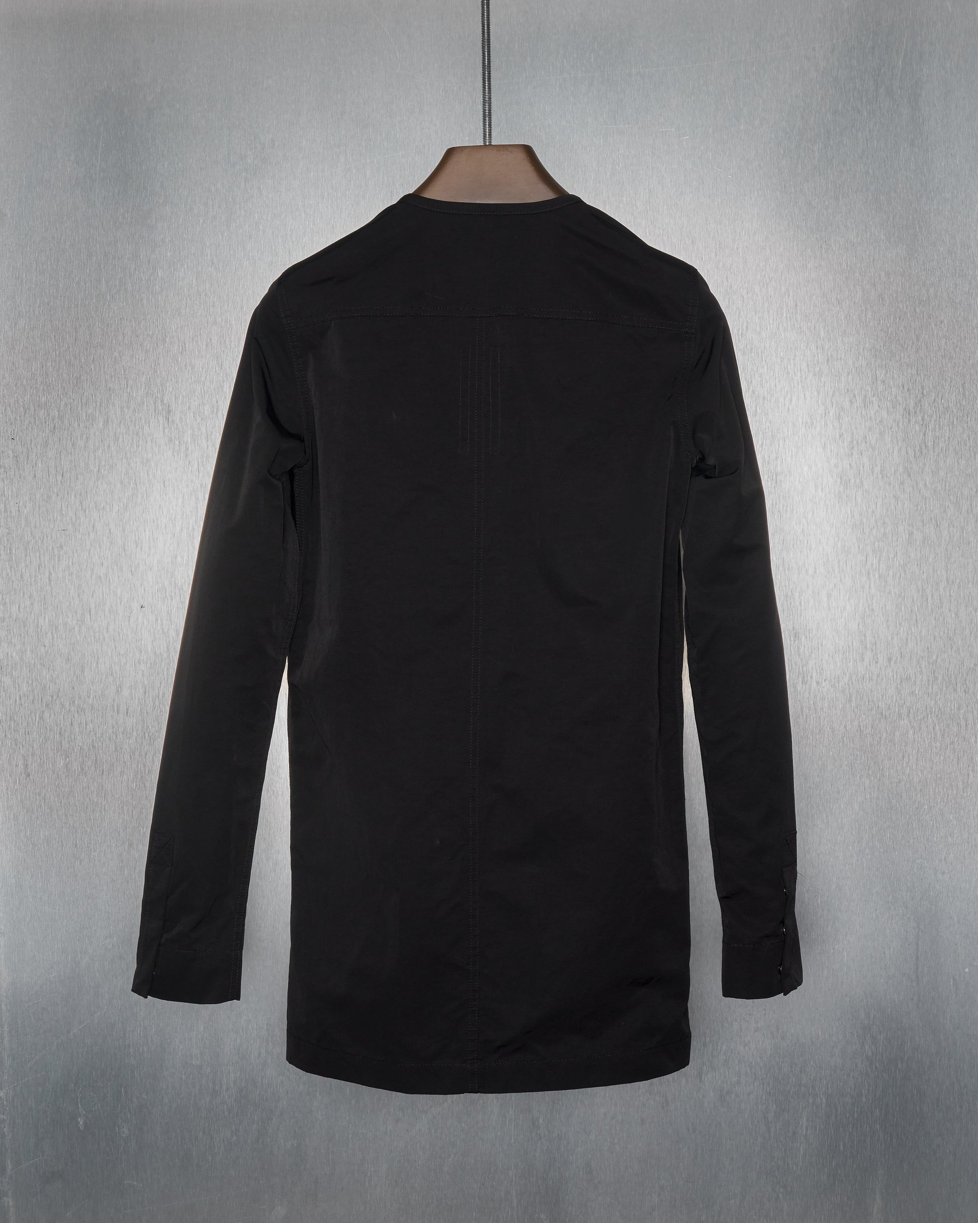 The reverse of a black Rick Owens zip-up collarless coat with an asymmetric front zip and a perforated breast pocket made from soft grained calfskin.