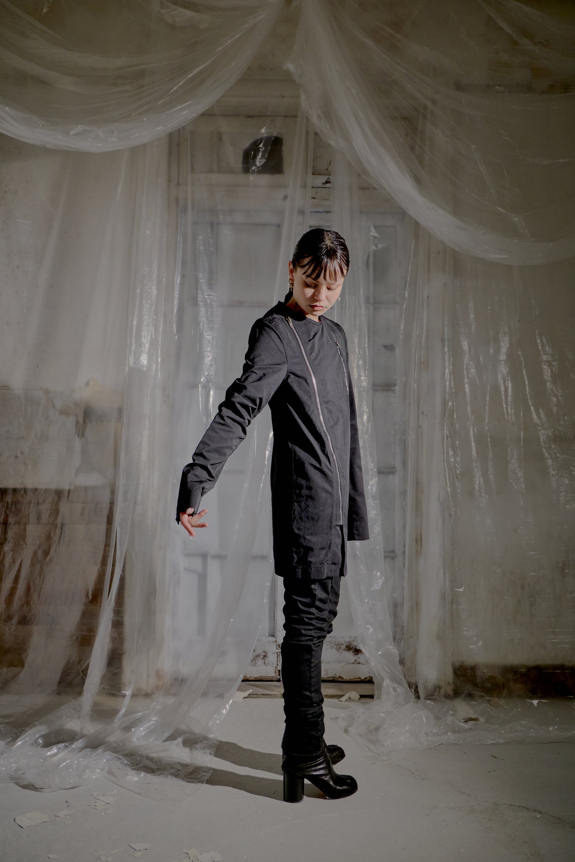 Person wearing a dark Rick Owens outfit standing in a room with draped fabric