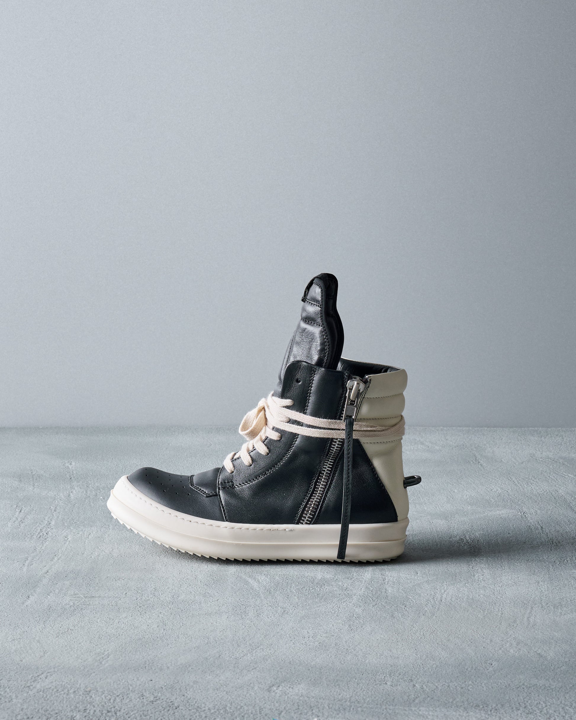 Black high-top Rick Owens sneaker with white sole on a gray background