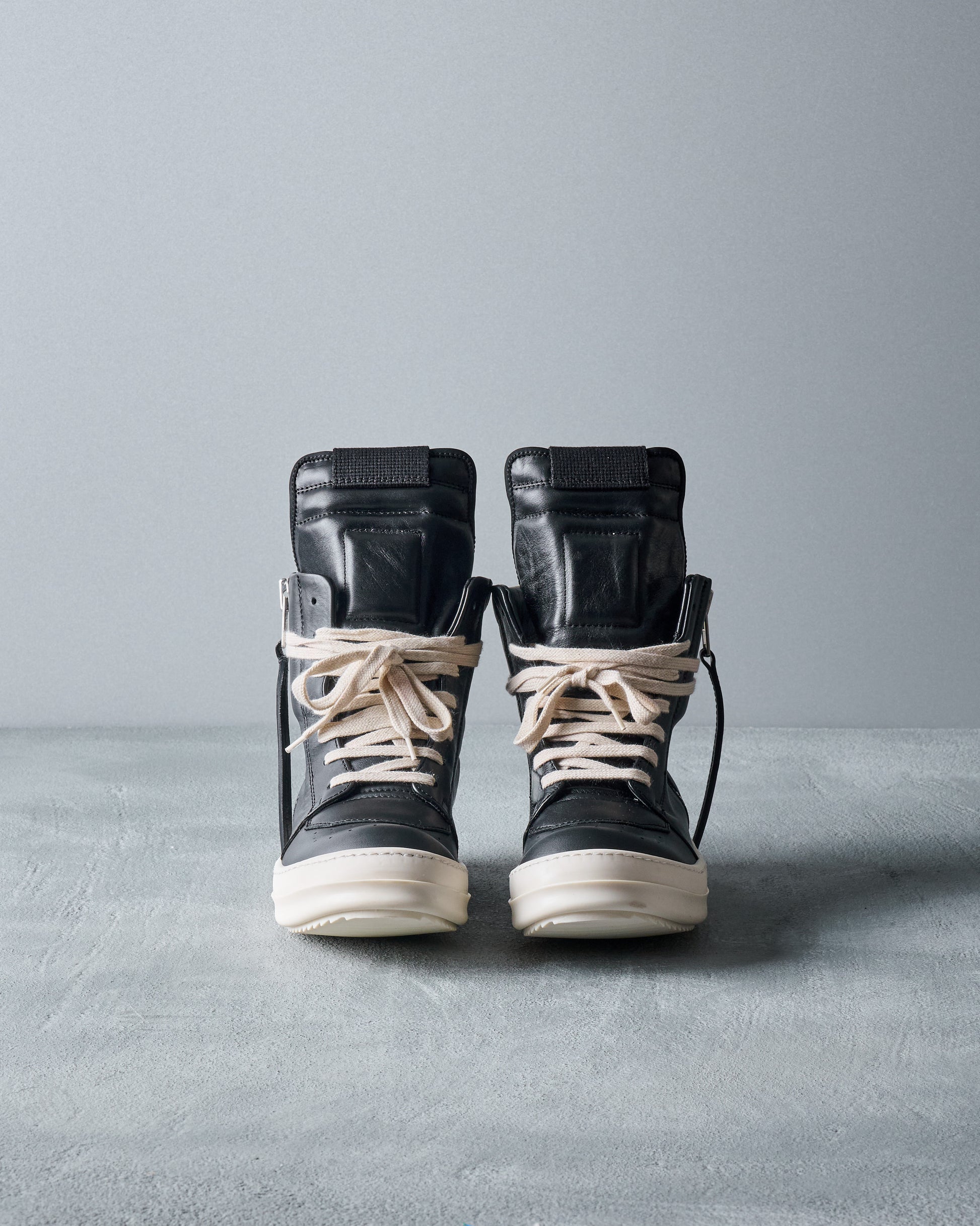 Pair of black high-top Rick Owens sneakers with white soles on a gray background