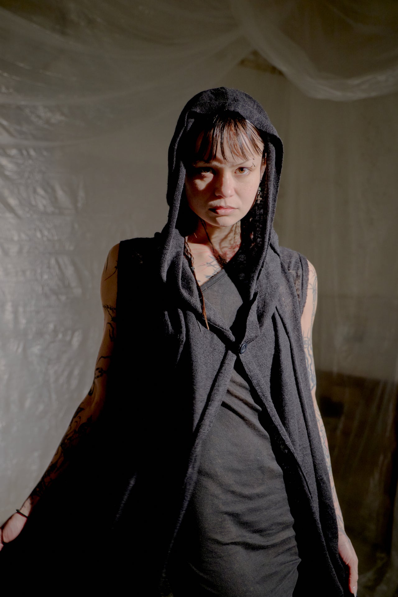 Person wearing a dark hooded Rick Owens garment against a textured white wall.