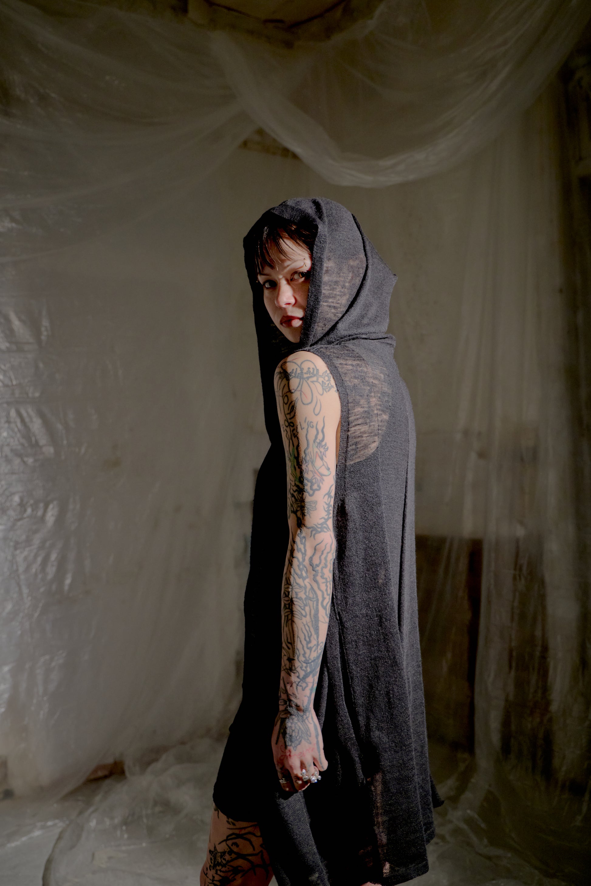 Person wearing a dark hooded Rick Owens cardigan garment in a softly lit room with draped fabric.