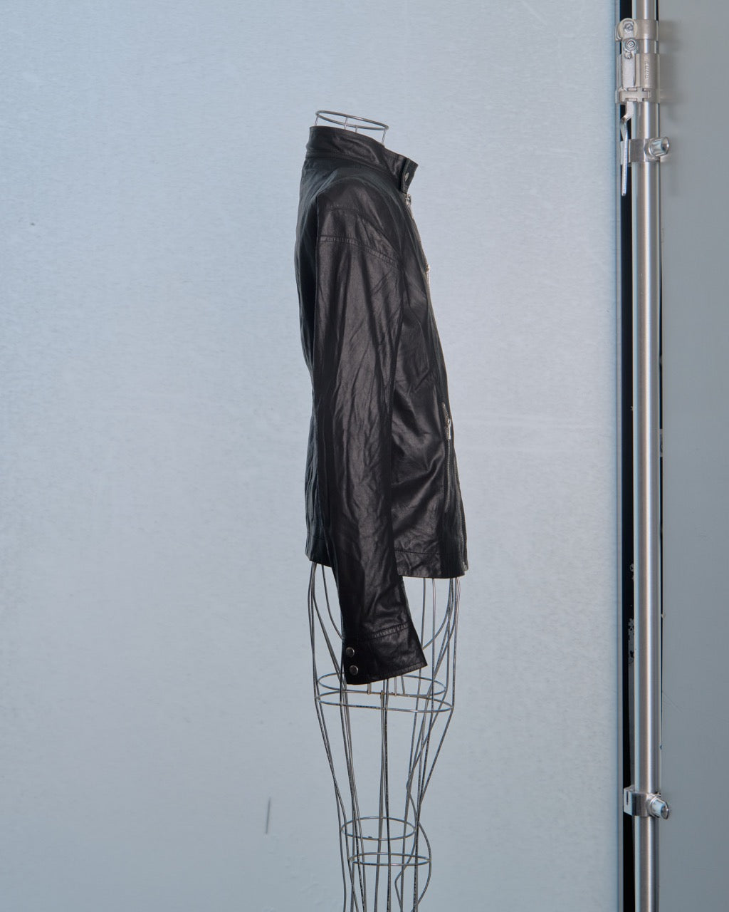 Black leather Rick Owens jacket on a wire mannequin against a light blue wall.