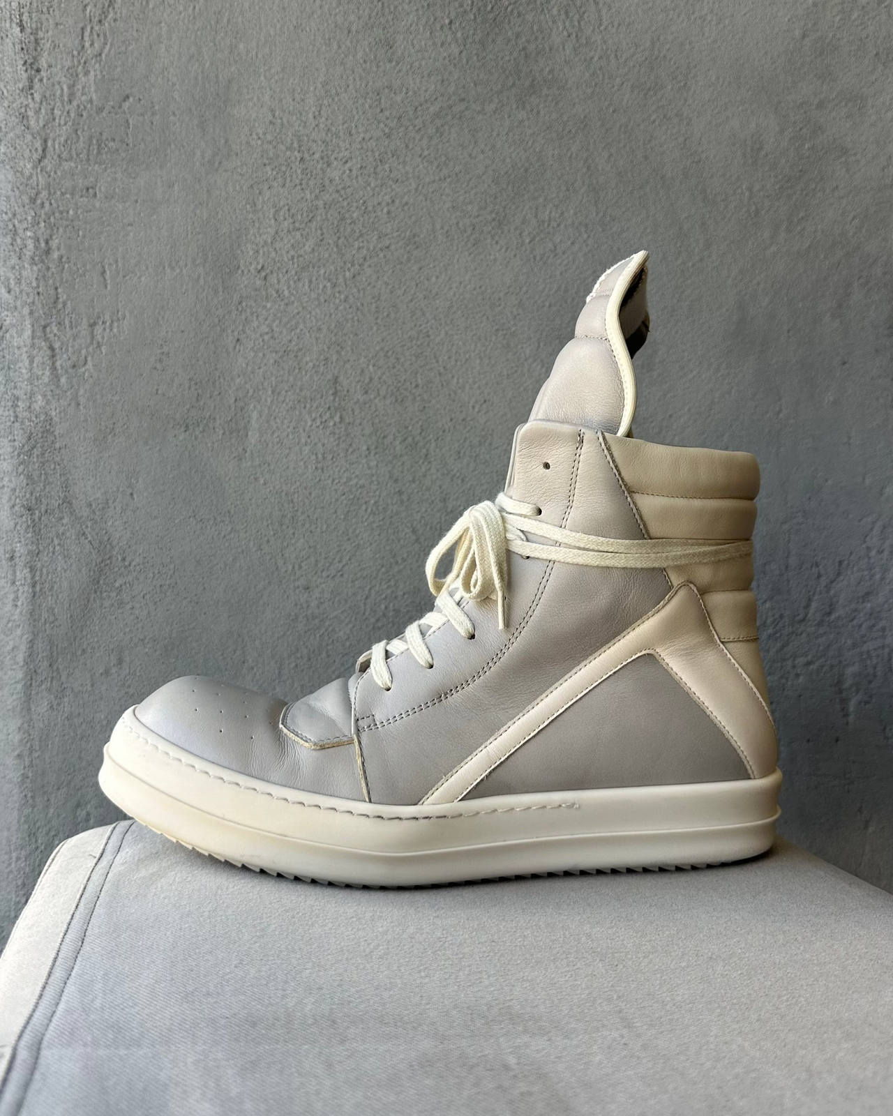 Gray high-top Rick Owens sneaker with white sole on a gray surface against a gray background