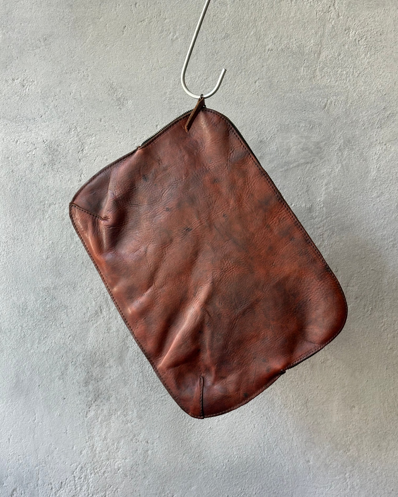 Brown leather Royal Republiq pouch hanging on a hook against a gray wall