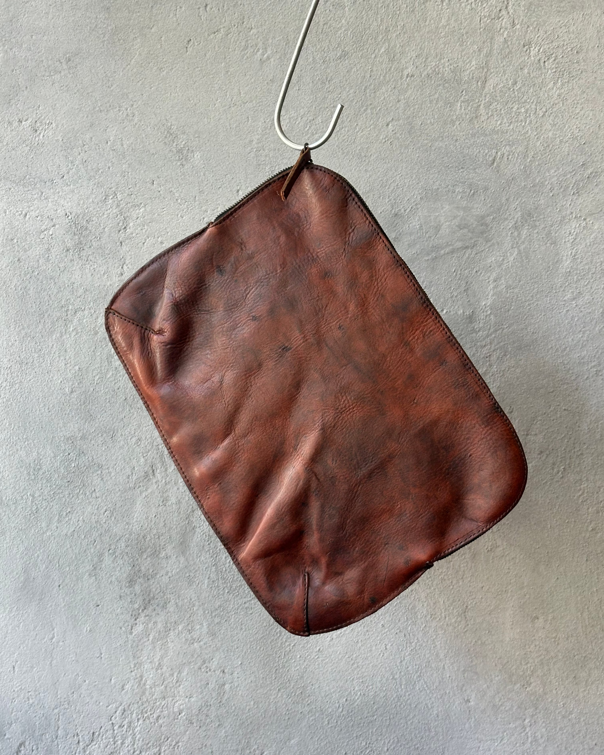 Brown leather Royal Republiq pouch hanging on a hook against a gray wall