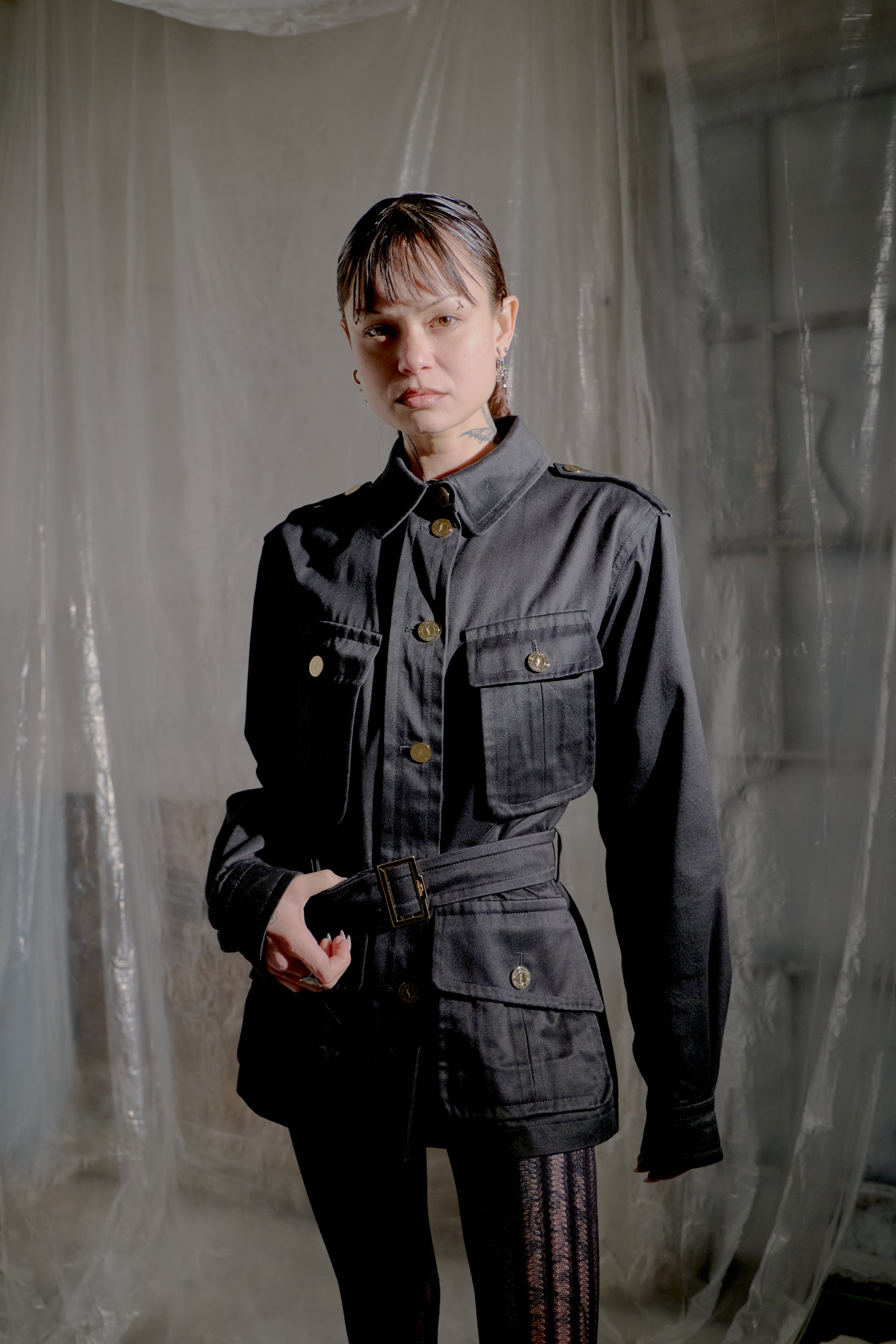Person wearing a dark Saint Laurent jacket standing in a softly lit room with sheer curtains.