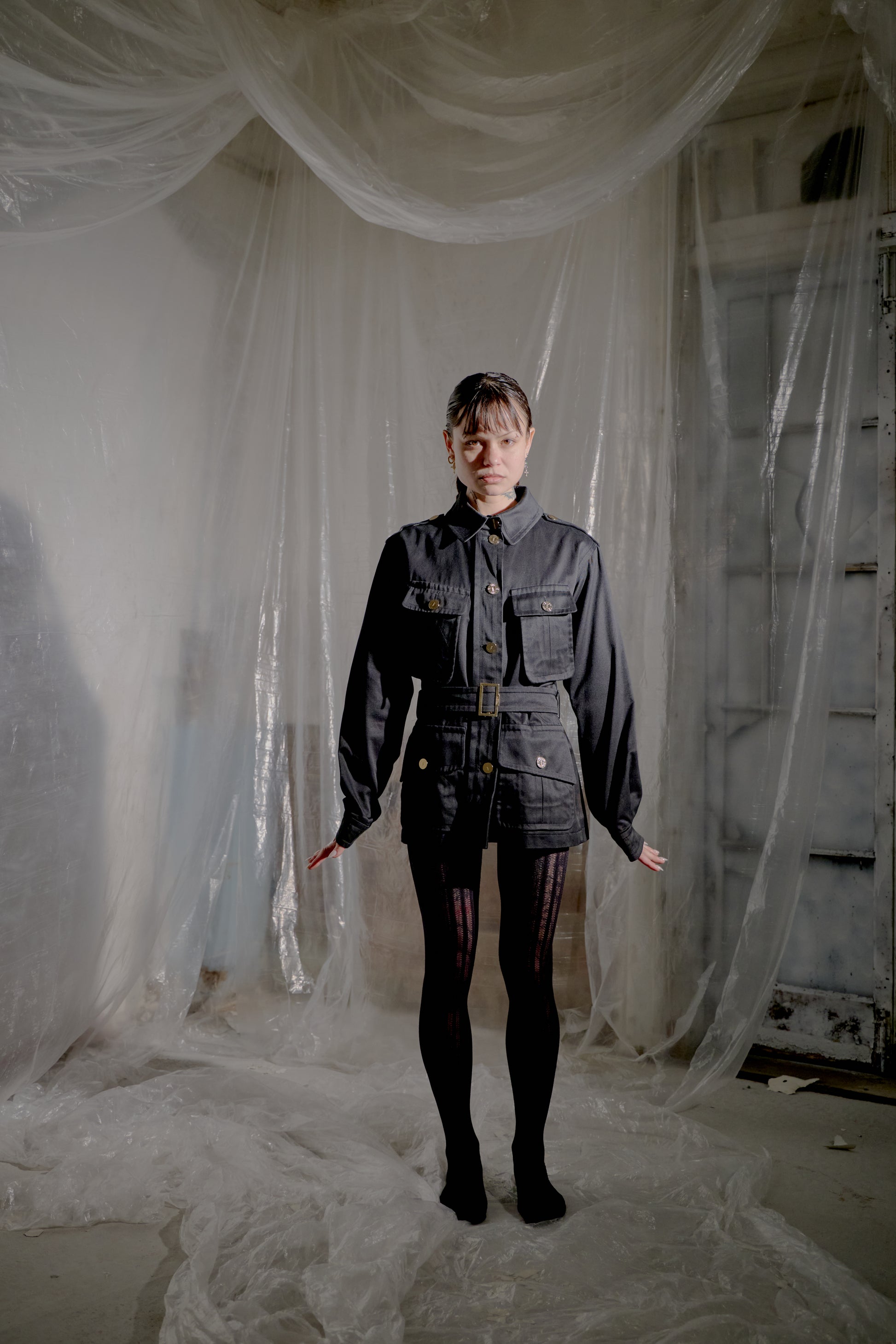 Person wearing a dark Saint Laurent jacket and pants standing in a room with white plastic sheeting.