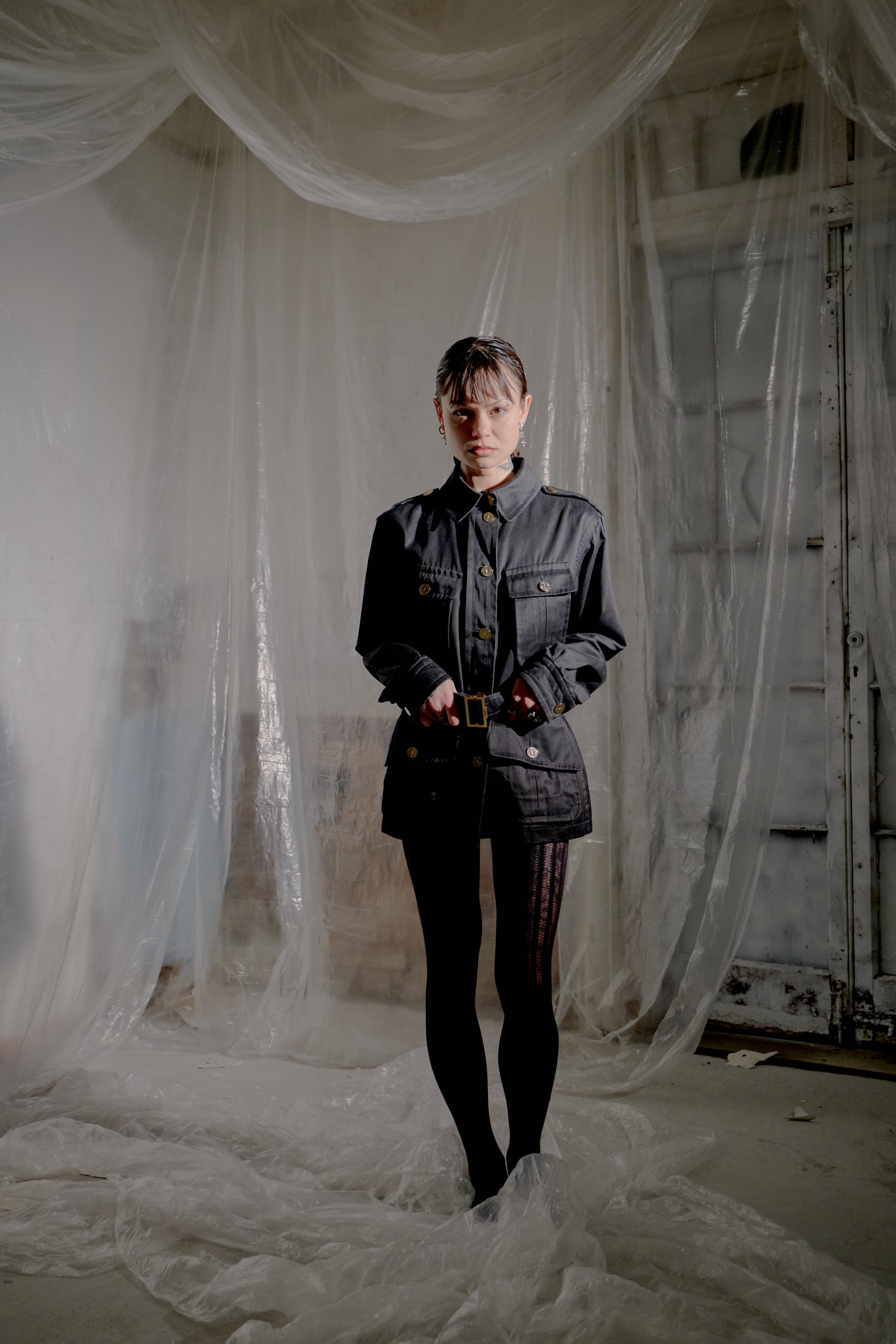 Person standing in a room with white fabric draped around, wearing a dark Saint Laurent outfit.