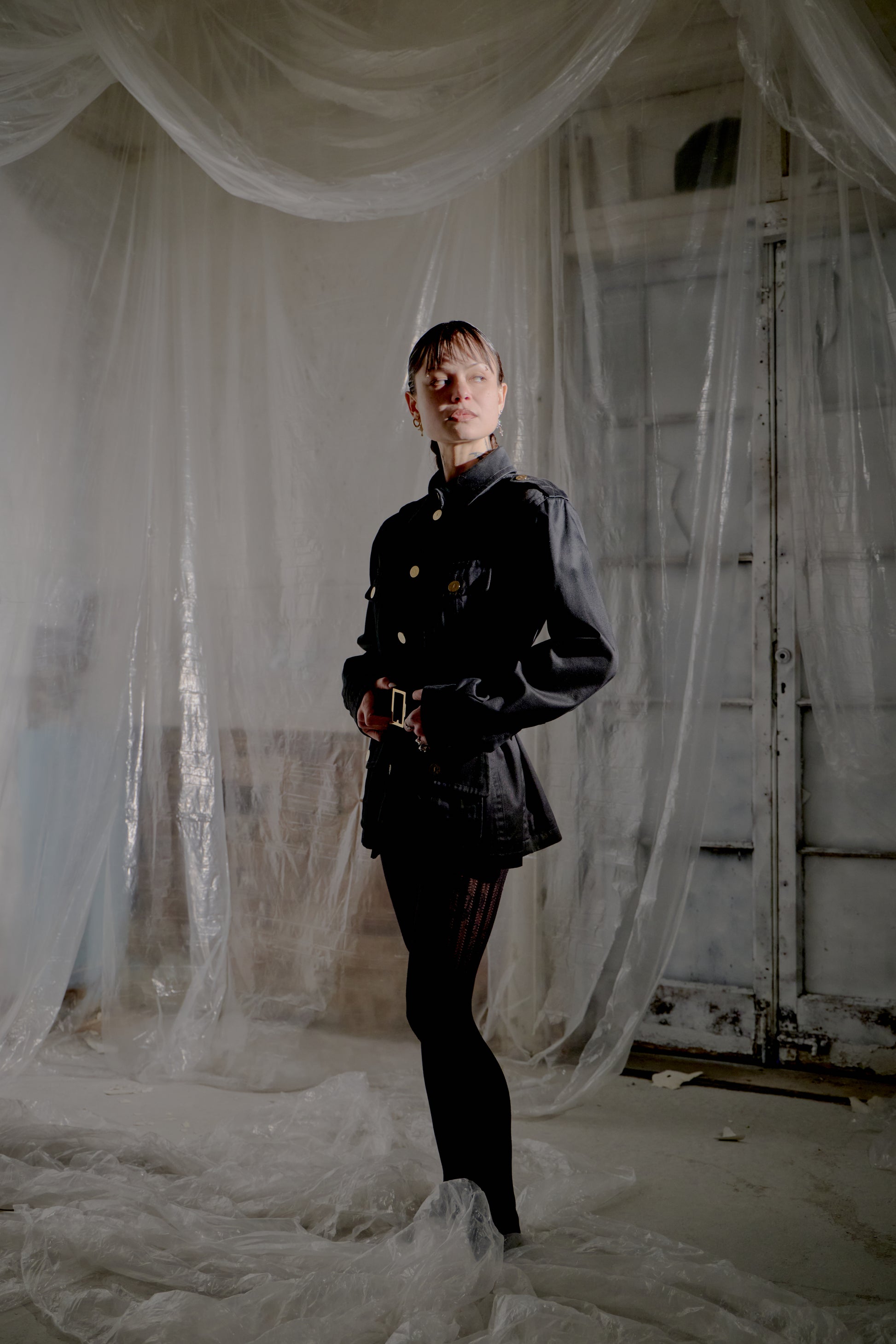 Person in a dark Saint Laurent outfit standing amidst draped white fabric in an industrial setting