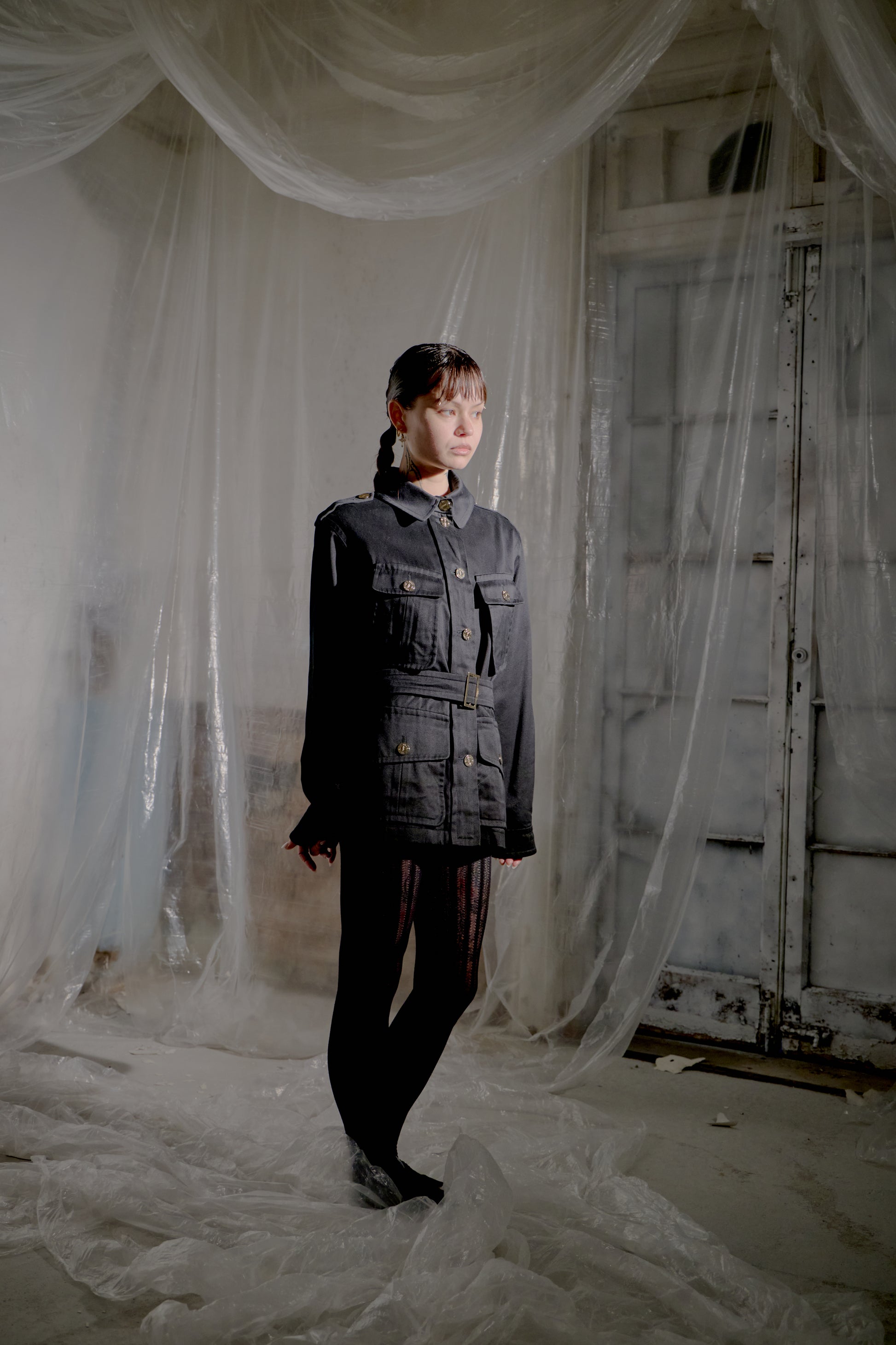 Person standing in a room wearing a black Saint Laurent jacket with sheer white curtains and a rustic door.