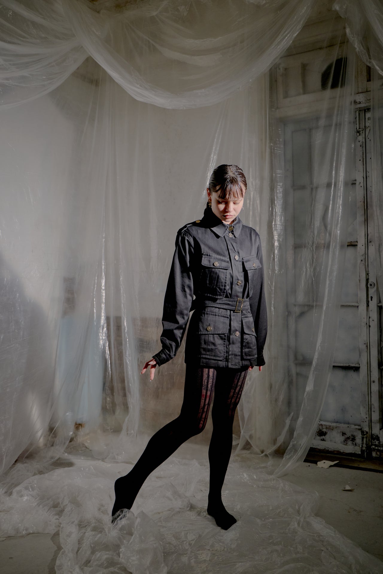 Person wearing a dark Saint Laurent jacket and pants standing in a room with white plastic sheeting.