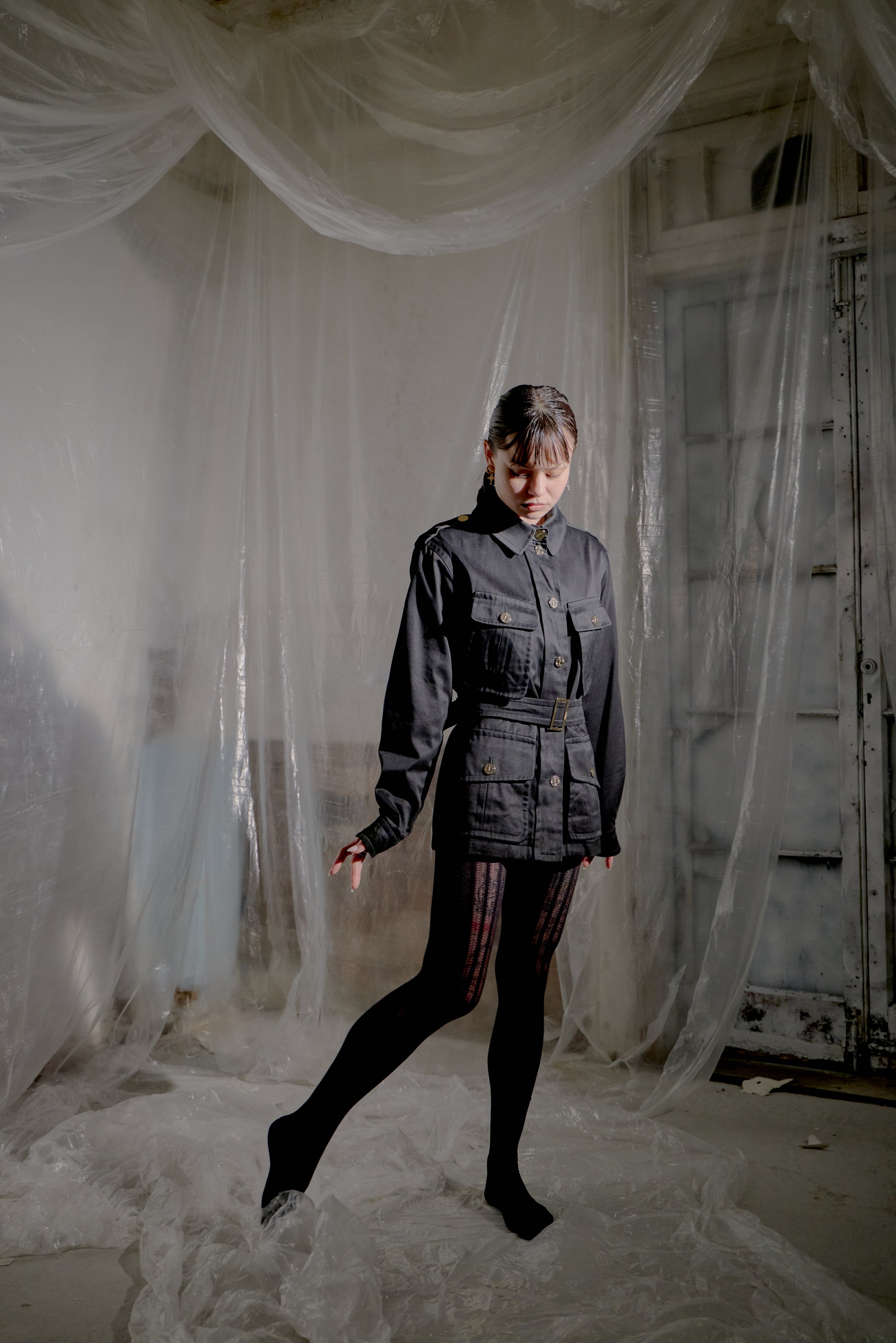 Person wearing a black Saint Laurent outfit standing in a room with white fabric draped around.