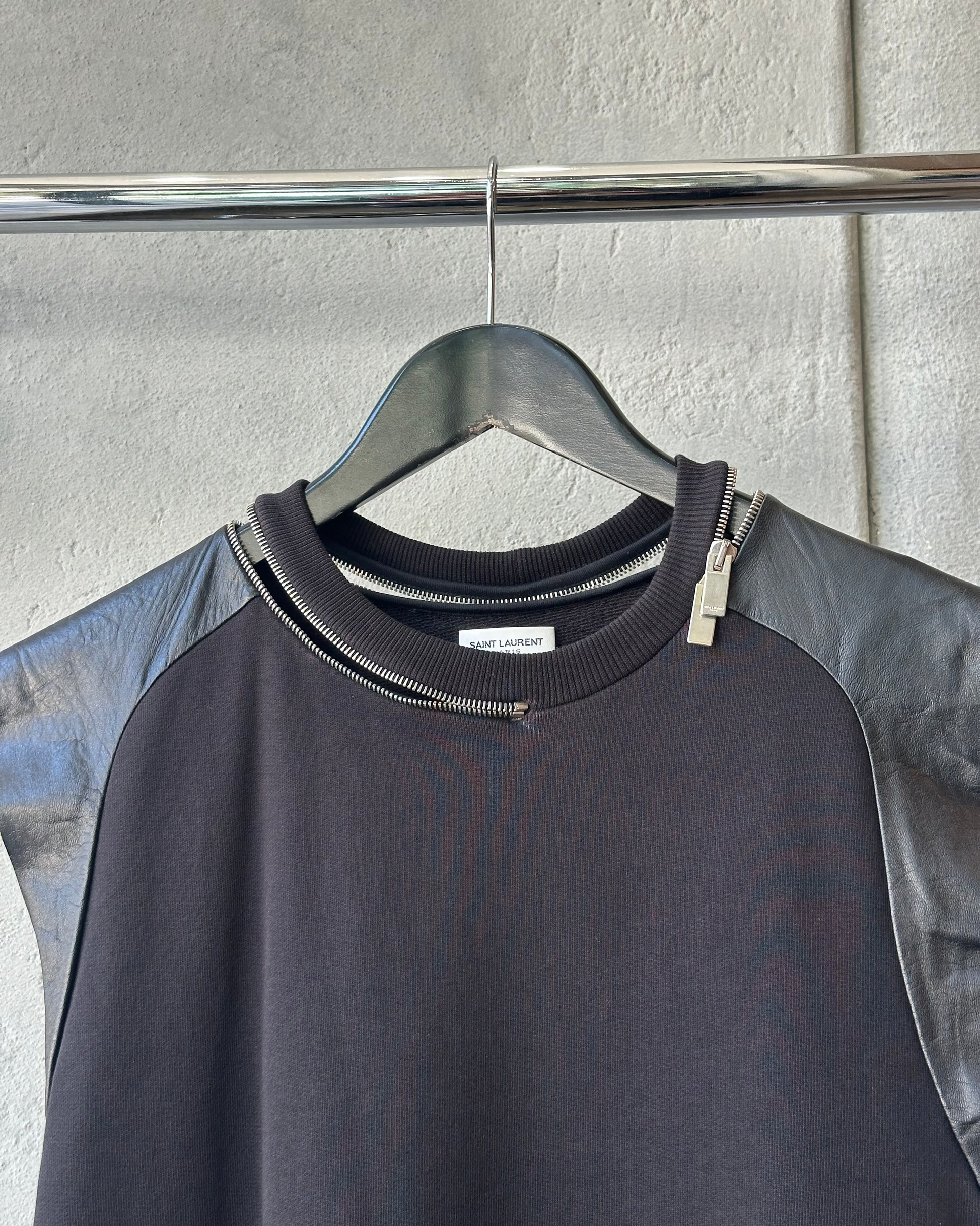 Black Saint Laurent tank top with zipper details on a hanger against a gray background