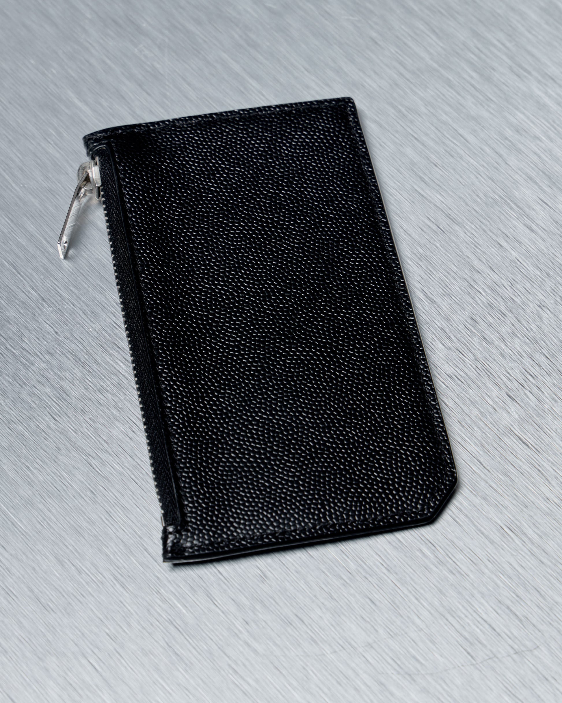 Black Saint Laurent leather zippered pouch on a gray textured surface