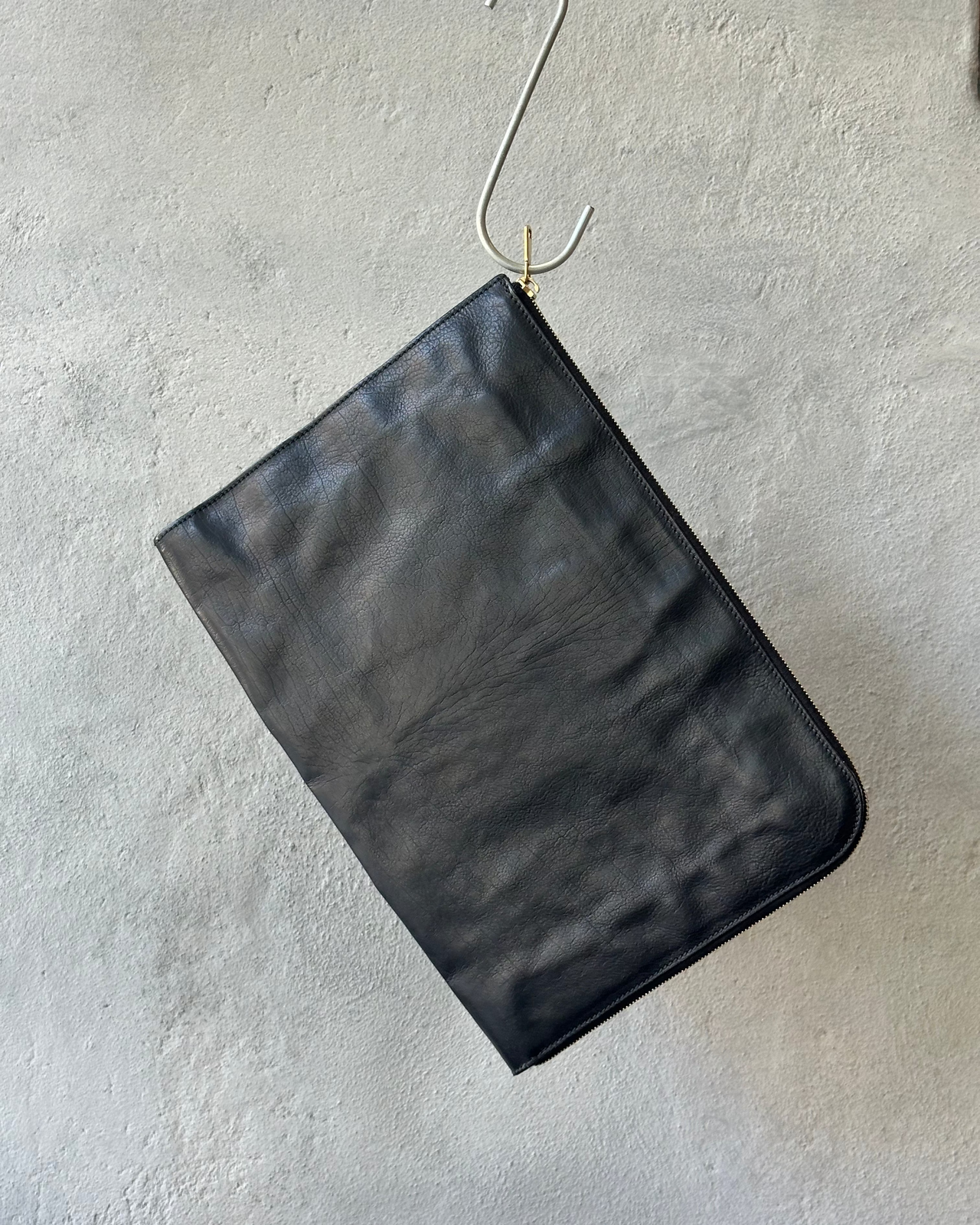 Black leather Saint Laurent clutch bag on a textured gray surface