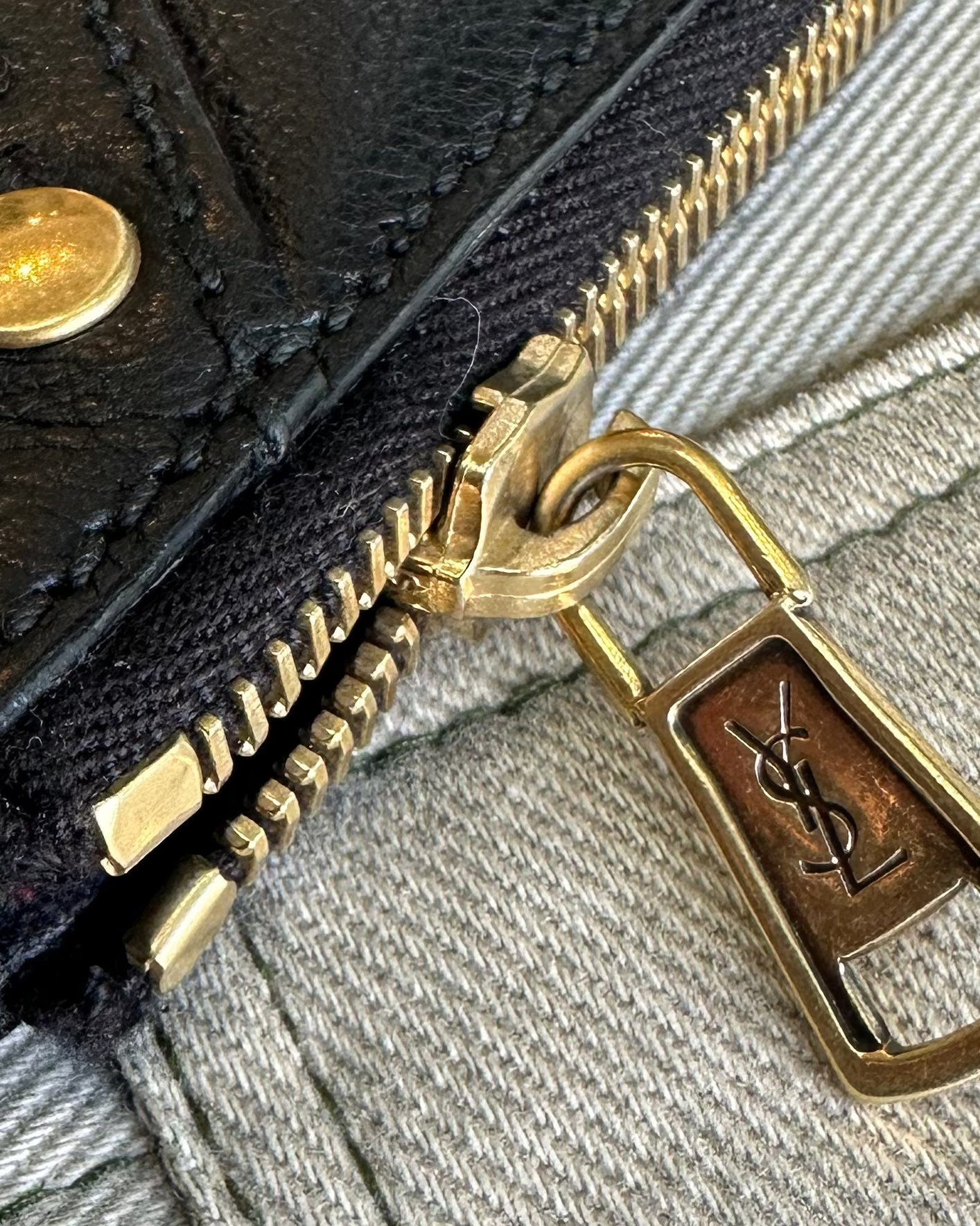 Close-up of a black leather Saint Laurent wallet with gold zipper and brand logo on a gray fabric background