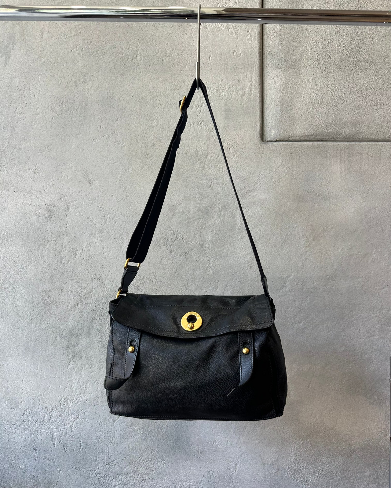Black Saint Laurent handbag with a gold clasp on a gray background