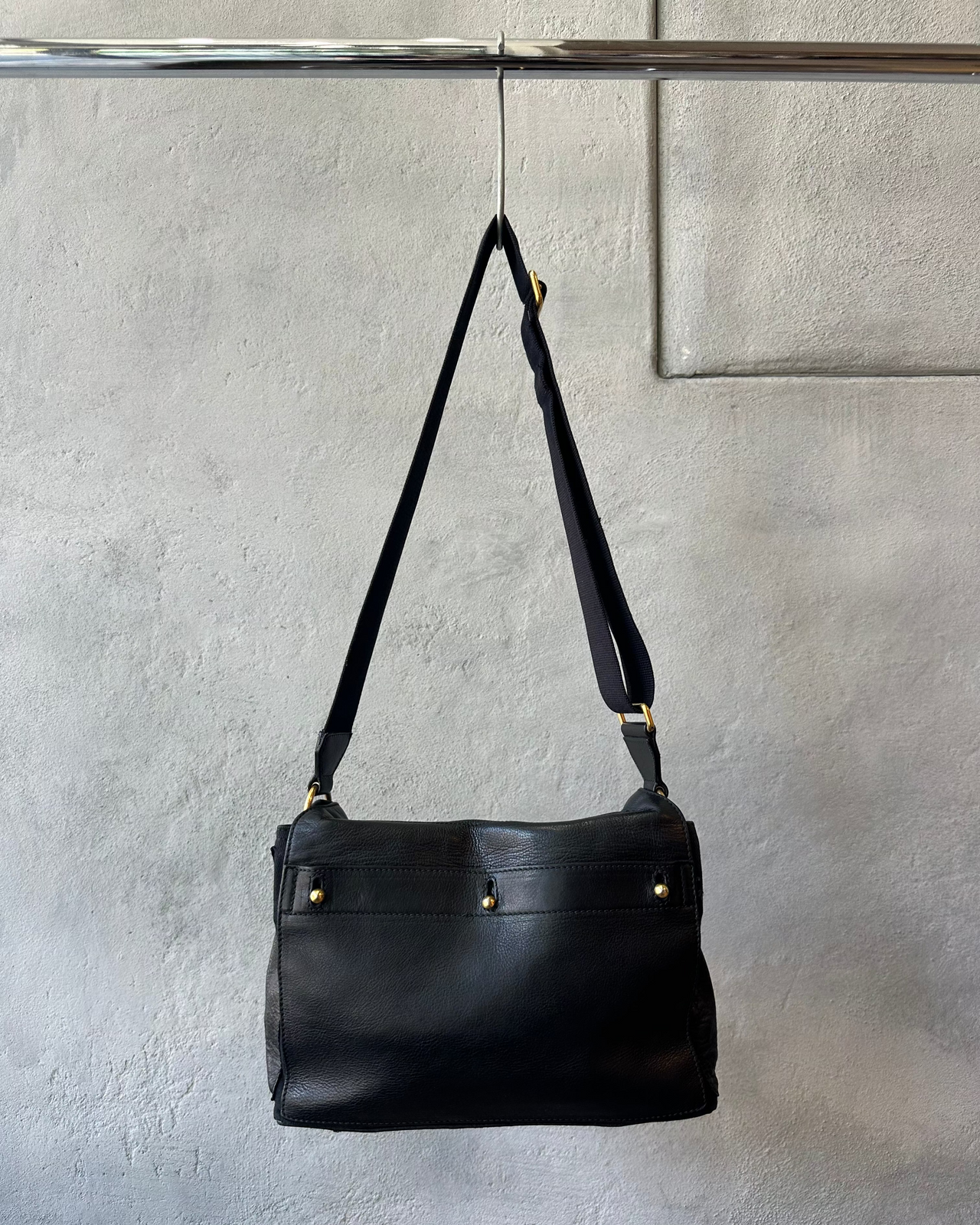 Black Saint Laurent handbag with a gold clasp on a gray background
