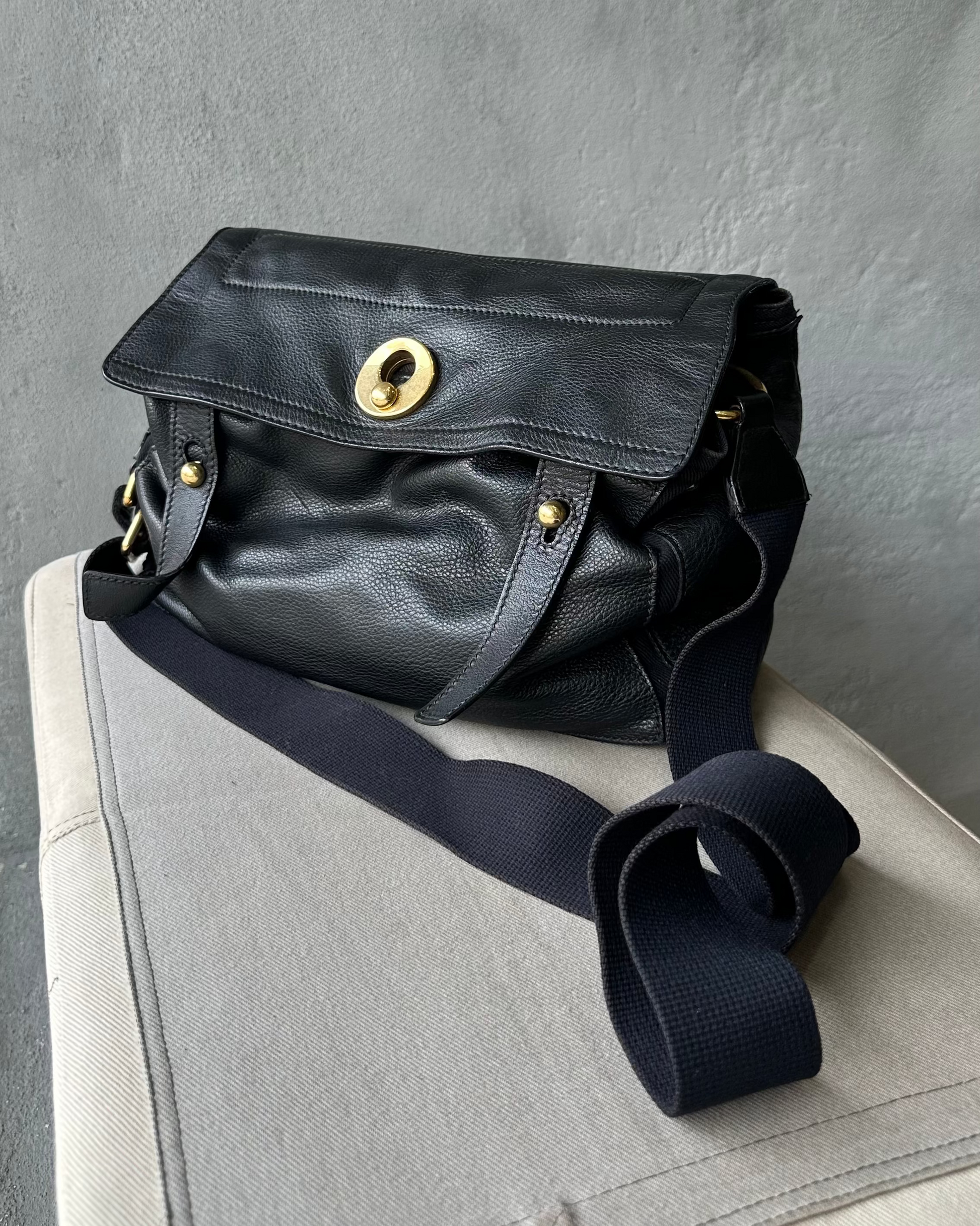 Black leather Saint Laurent bag with a gold buckle on a gray surface