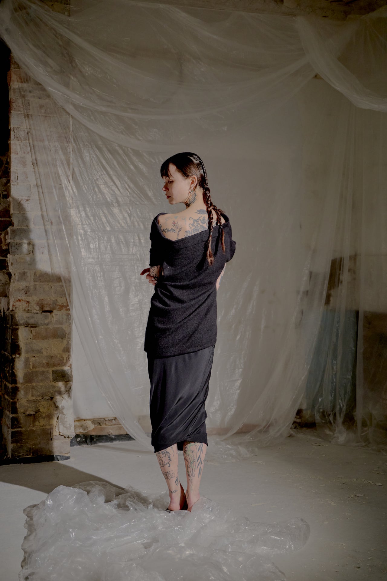 Woman in a black off-shoulder Saint Laurent dress standing in a room with white fabric draped on the wall.