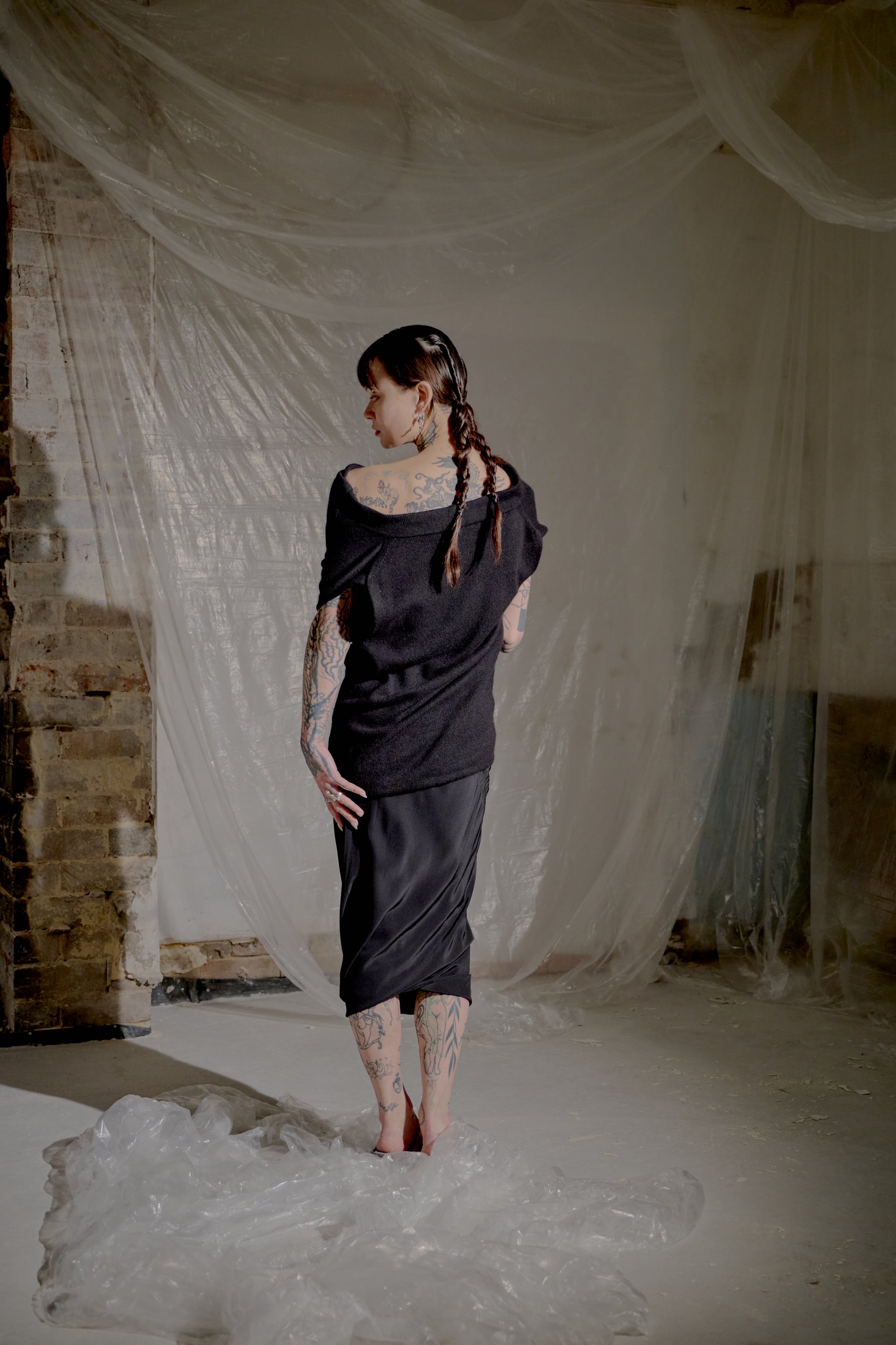 Woman in a black Saint Laurent top standing in a room with white fabric and brick walls.