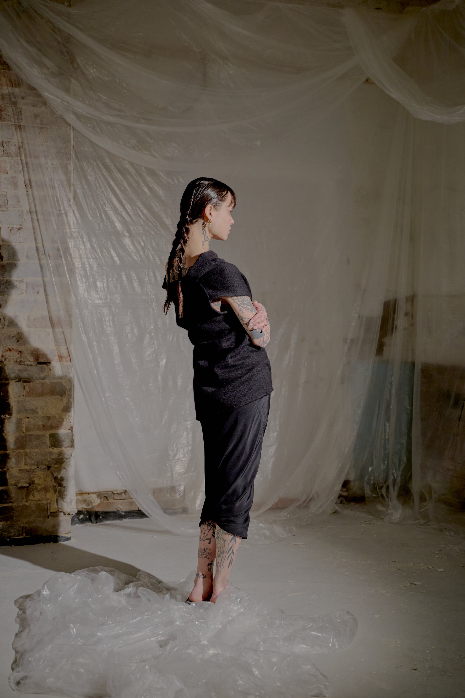 Person standing in a room with white fabric draped around, wearing a black Saint Laurent outfit.