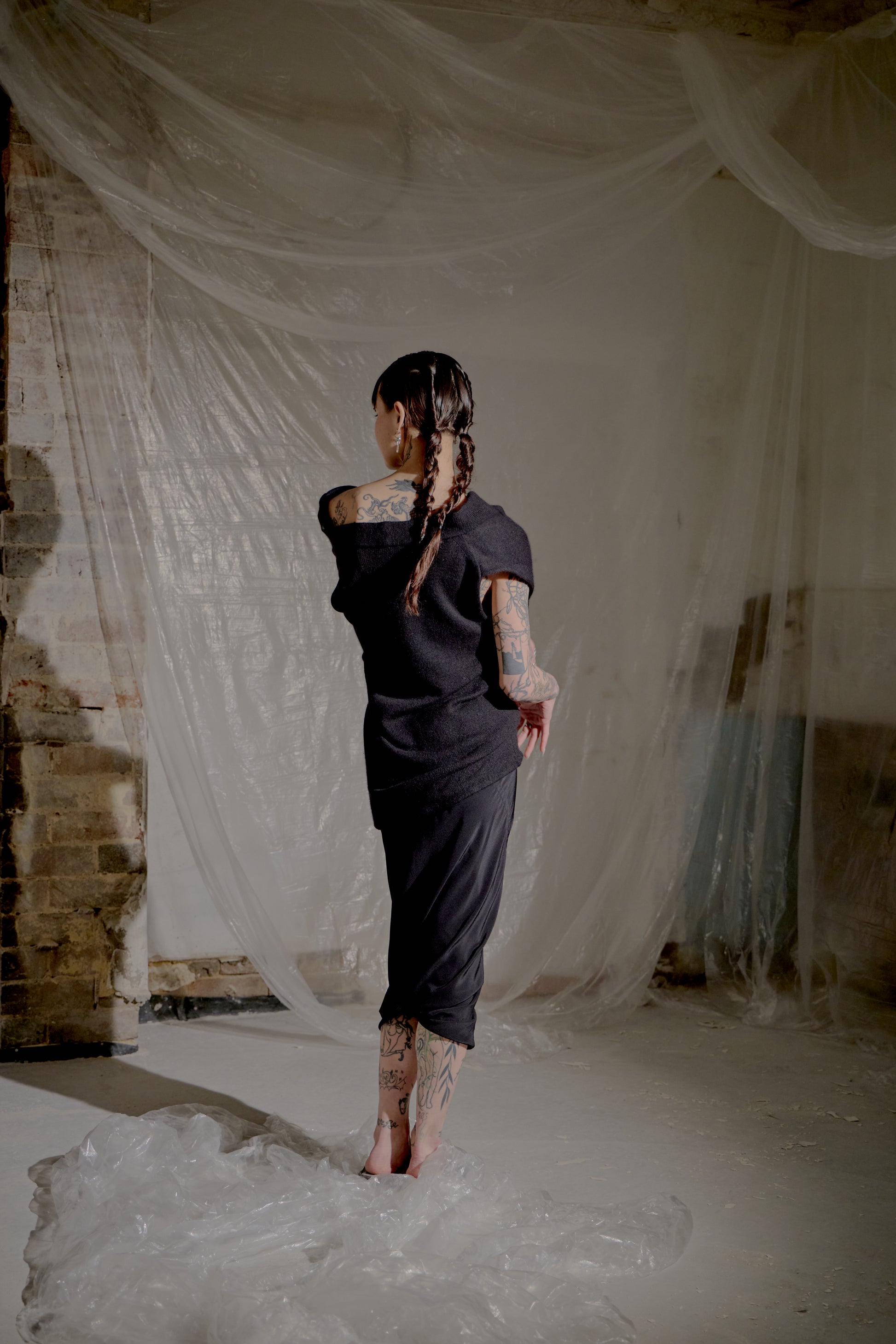 Person in a black Saint Laurent top standing in a room with white fabric draped around