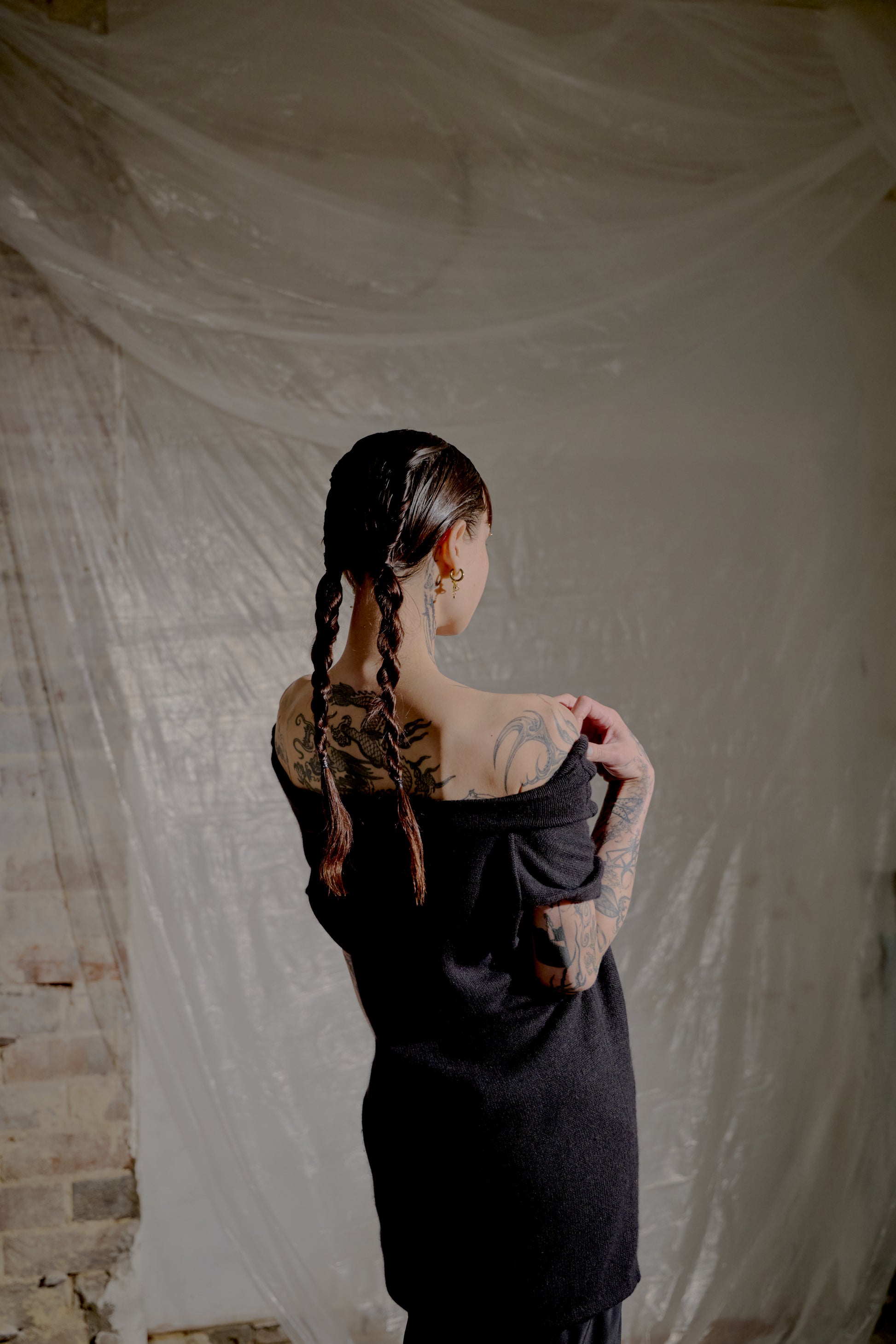 Person with braided hair and tattoos wearing a black Saint Laurent top in an indoor setting.