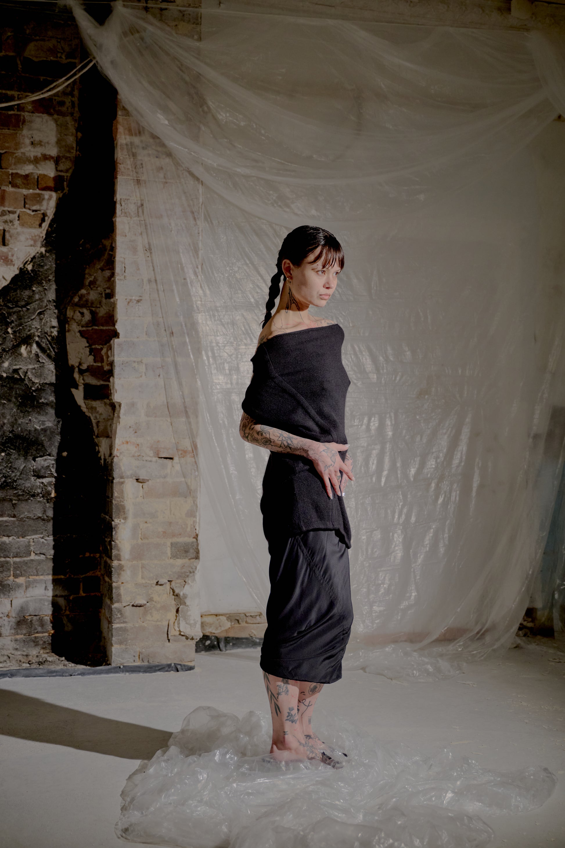 Person in a dark Saint Laurent outfit standing in water with a draped white cloth in the background