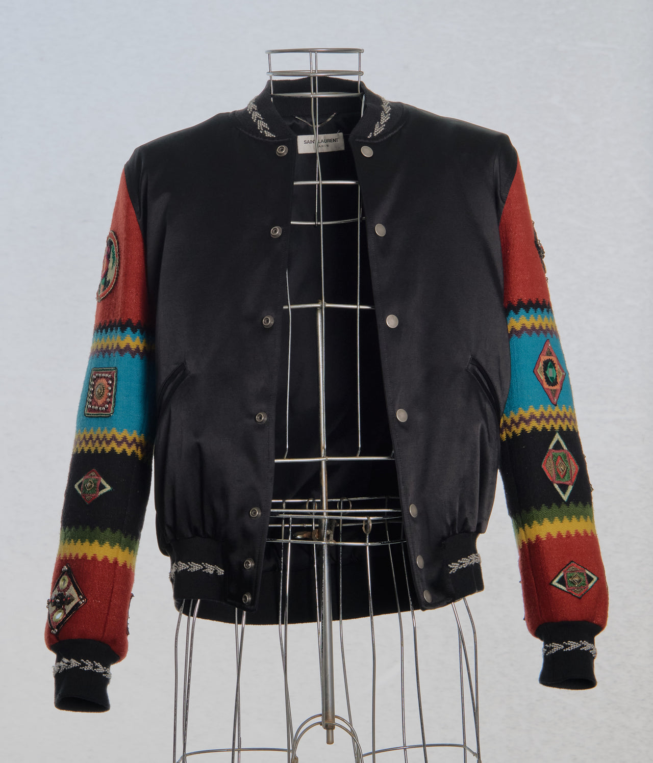 Black Saint Laurent jacket with colourful patterned sleeves on a mannequin against a light gray background