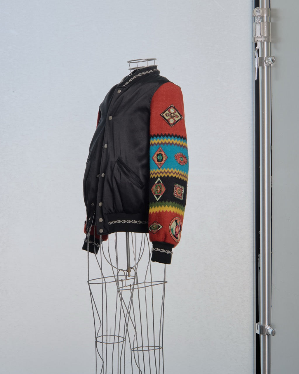 Black Saint Laurent jacket with colorful patterned sleeves on a mannequin against a gray background