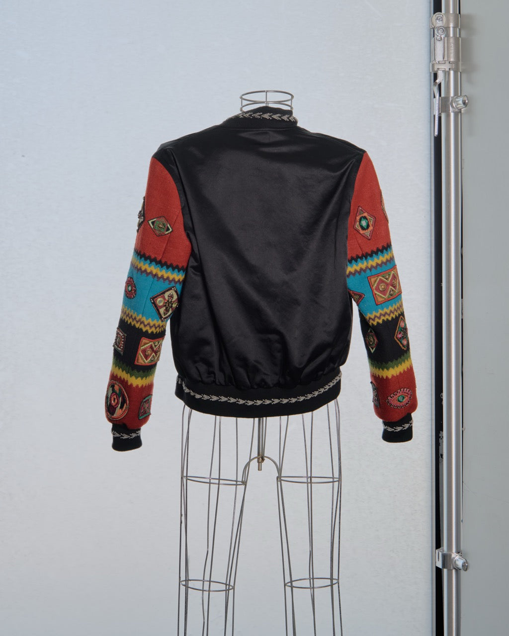 Black Saint Laurent jacket with colourful patterned sleeves on a mannequin against a light gray background