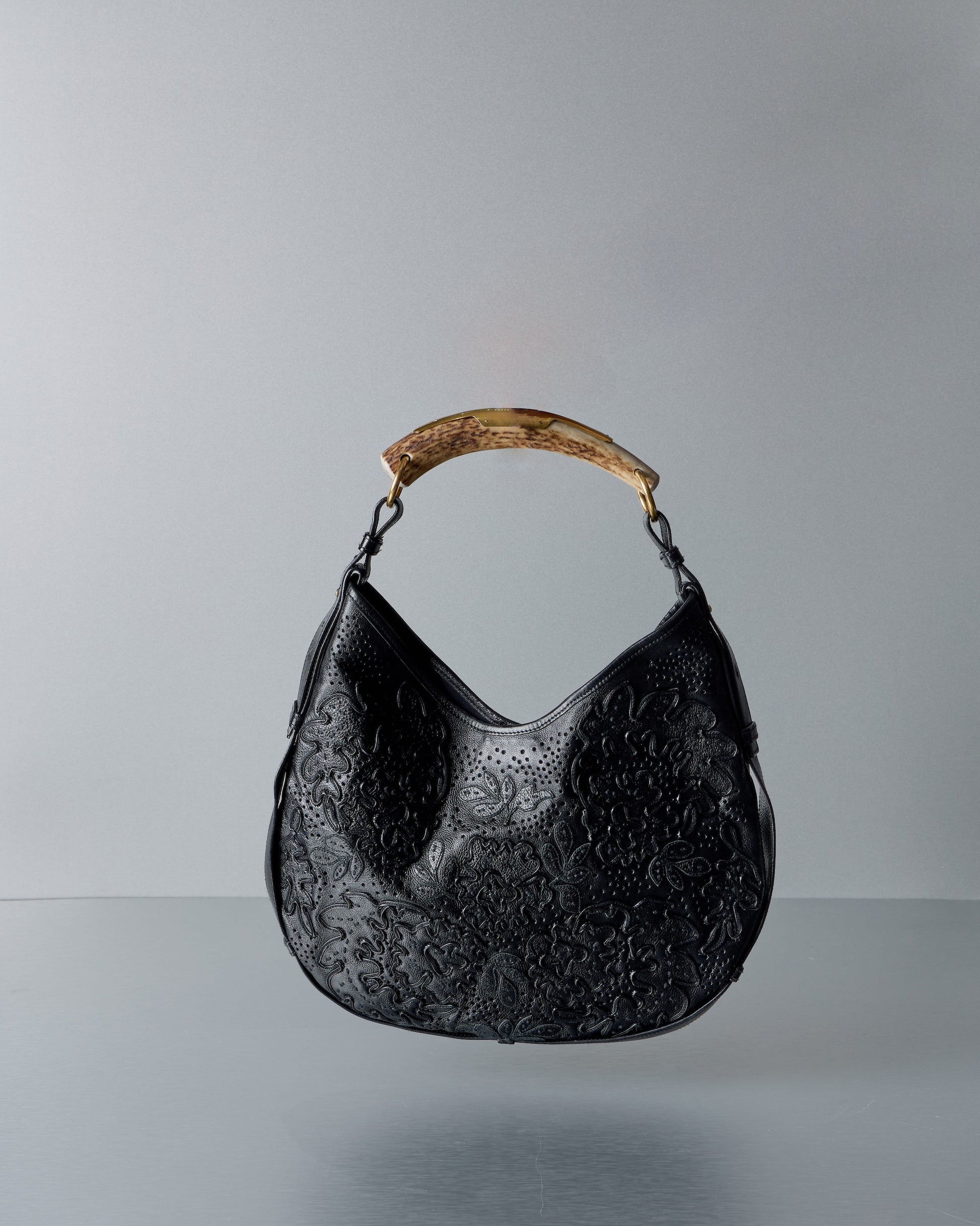 Black textured Saint Laurent Mombasa handbag with a gold handle on a gray background