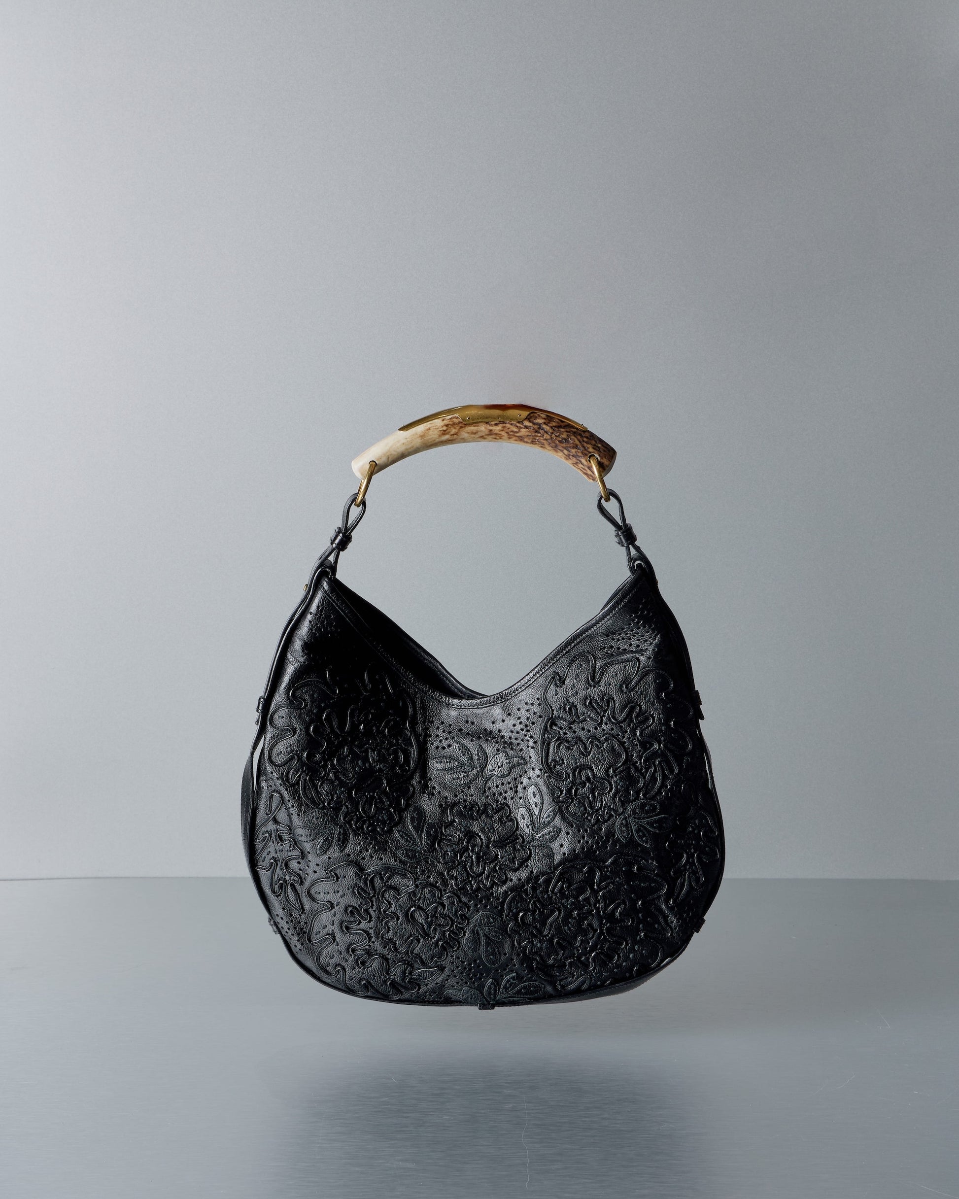Black textured Saint Laurent Mombasa handbag with a wooden handle on a gray background