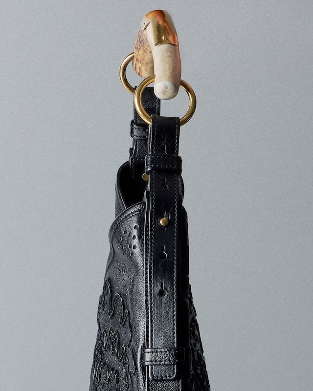 Black leather Saint Laurent Mombasa handbag with gold clasp on a gray background