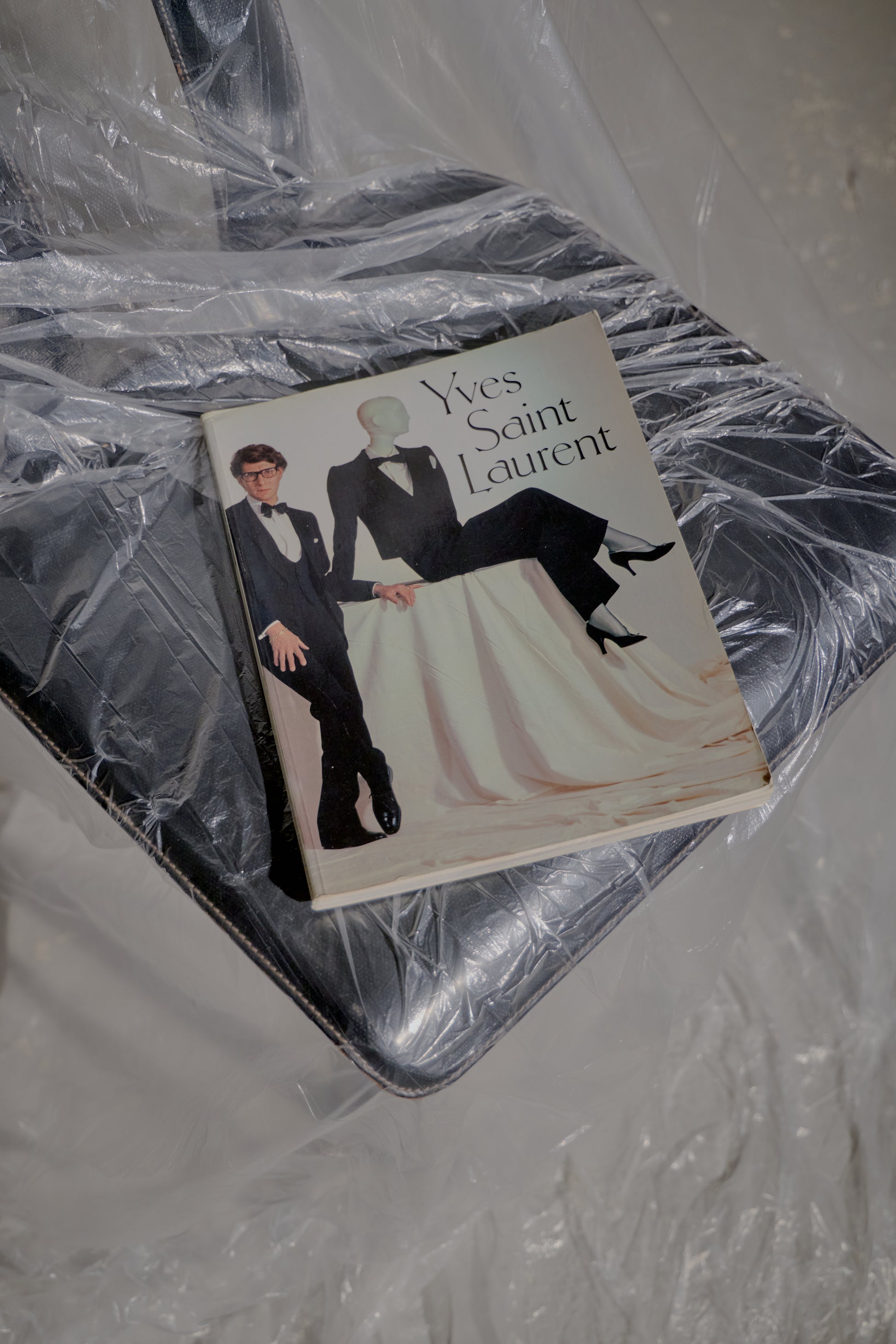 Yves Saint Laurent book on a plastic-wrapped black chair. The cover features two figures in formal attire, conveying elegance and sophistication.