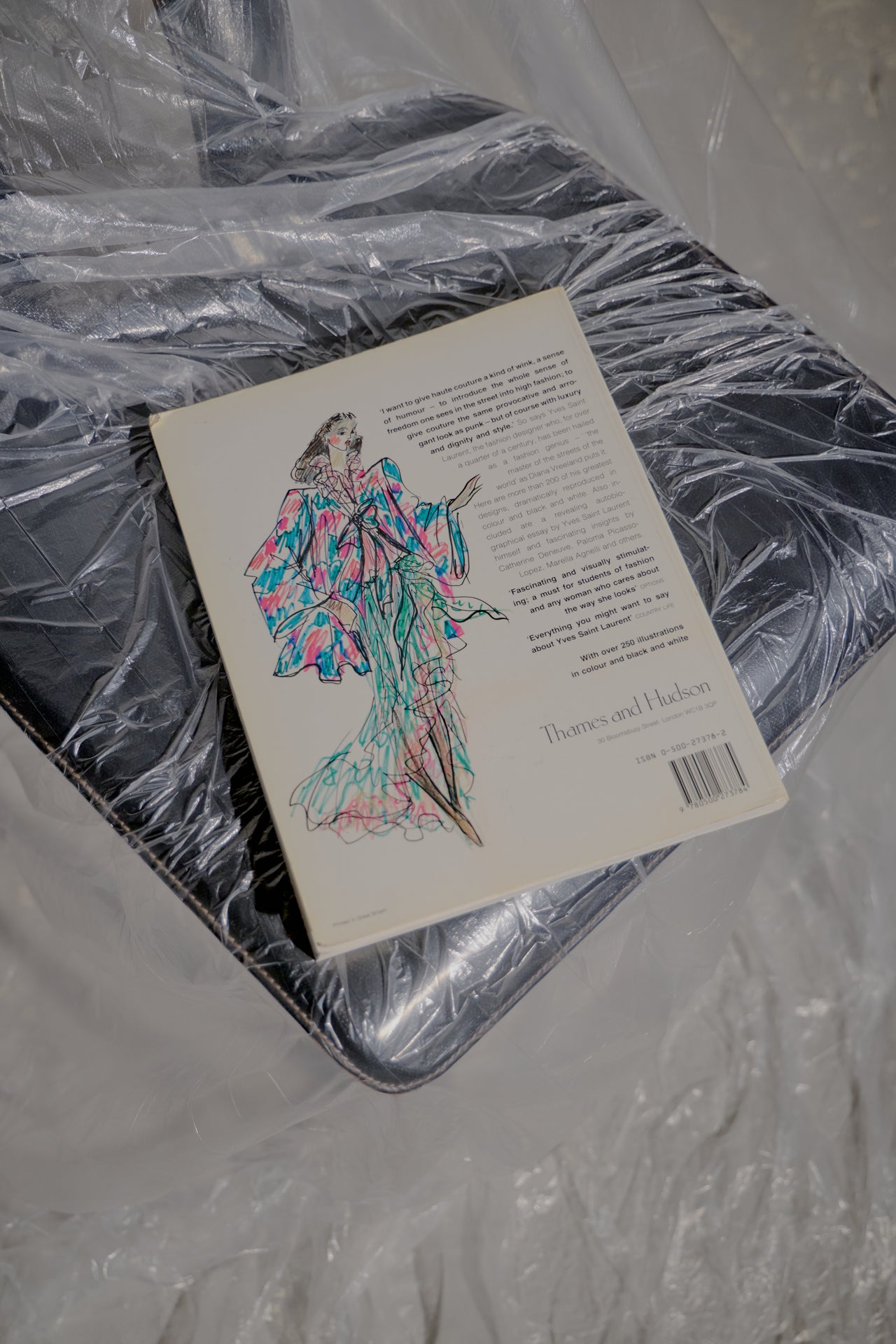 Yves Saint Laurent book on a plastic-wrapped black chair. The cover features two figures in formal attire, conveying elegance and sophistication.