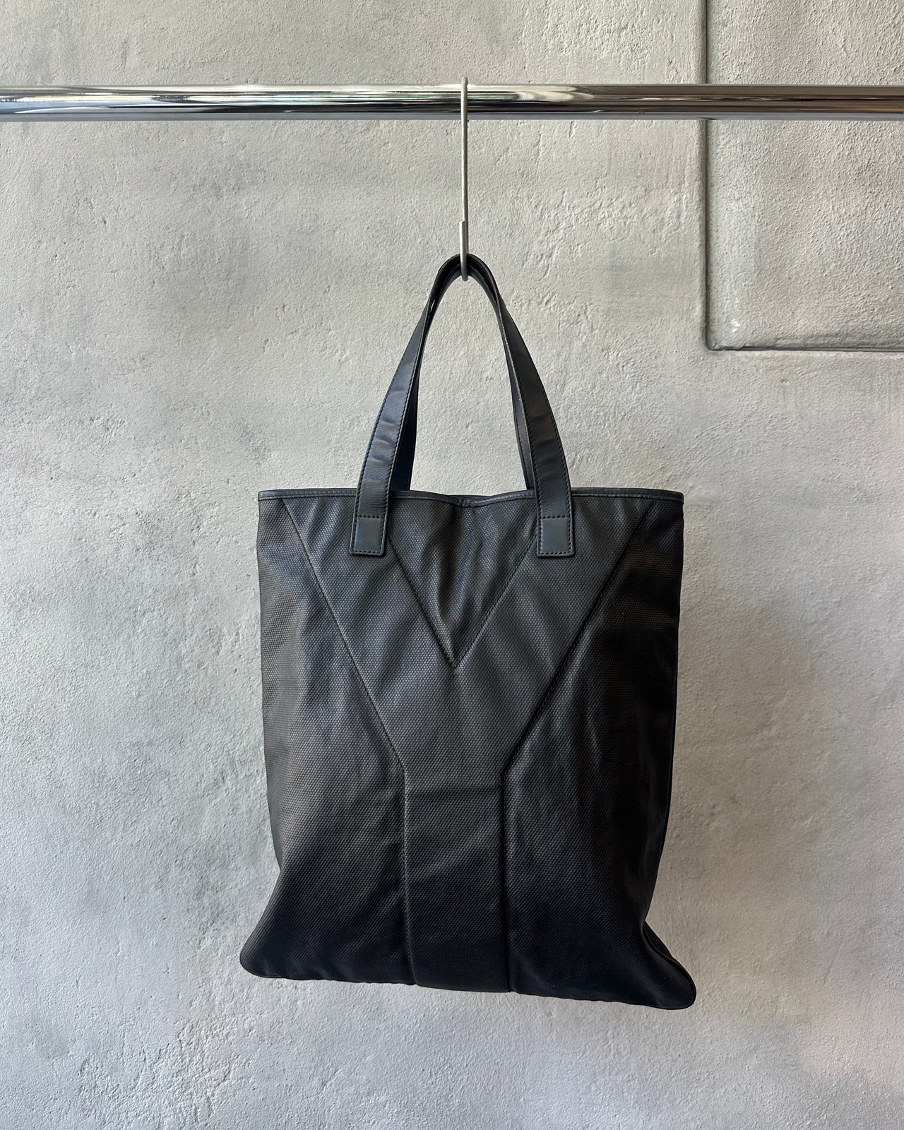 Black Saint Laurent tote bag hanging on a rack against a neutral wall