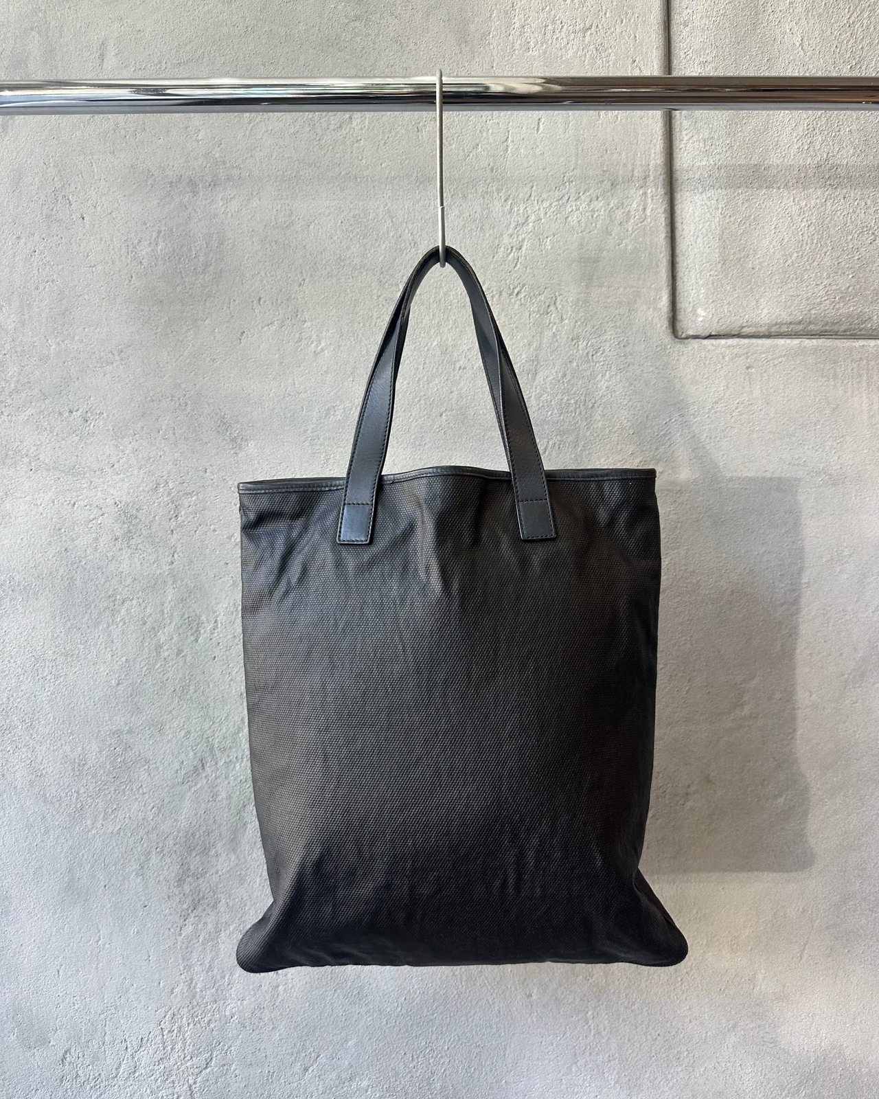 Black Saint Laurent tote bag hanging on a rack against a neutral wall