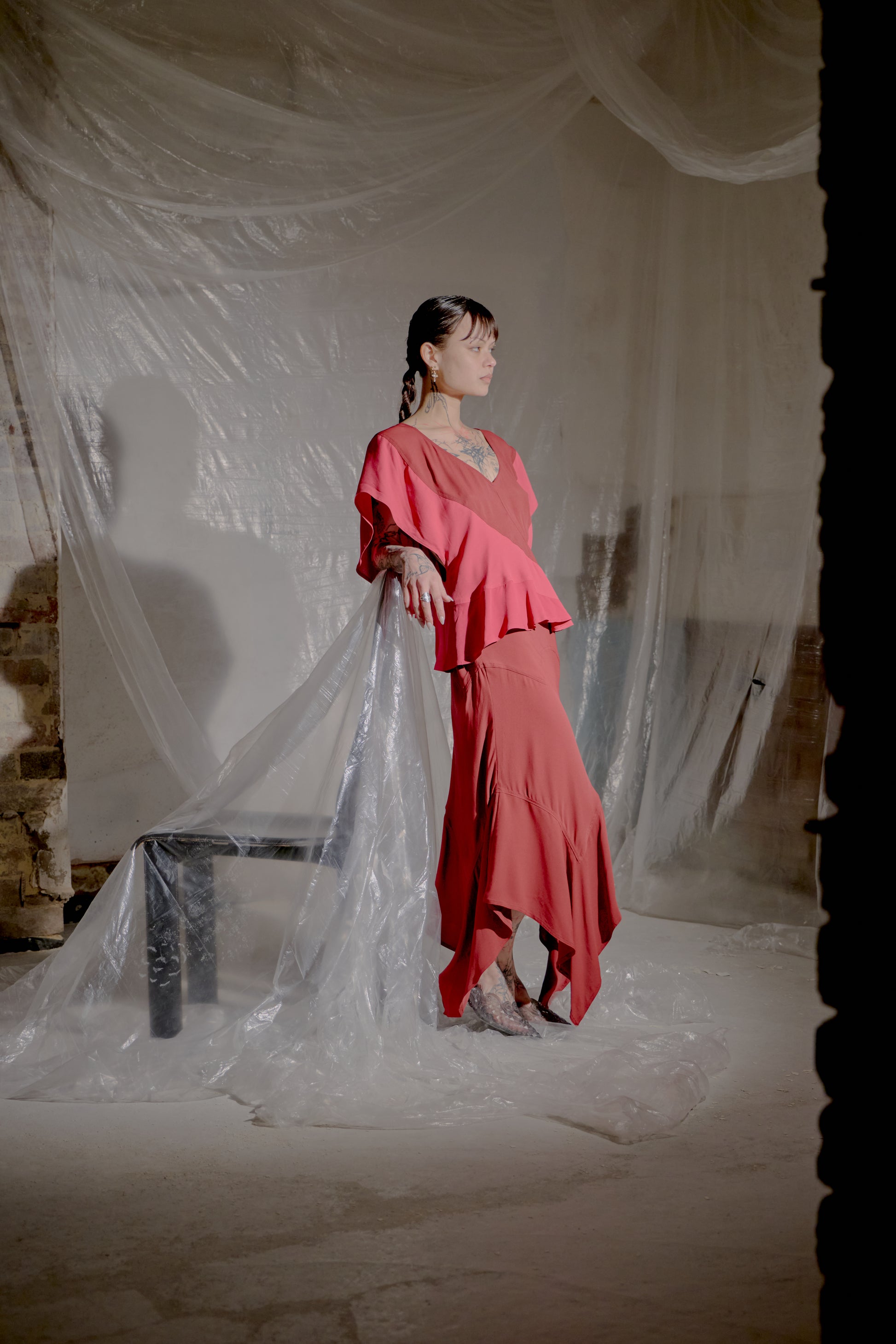 Woman in a red Saint Laurent outfit standing behind a draped white fabric in an indoor setting.