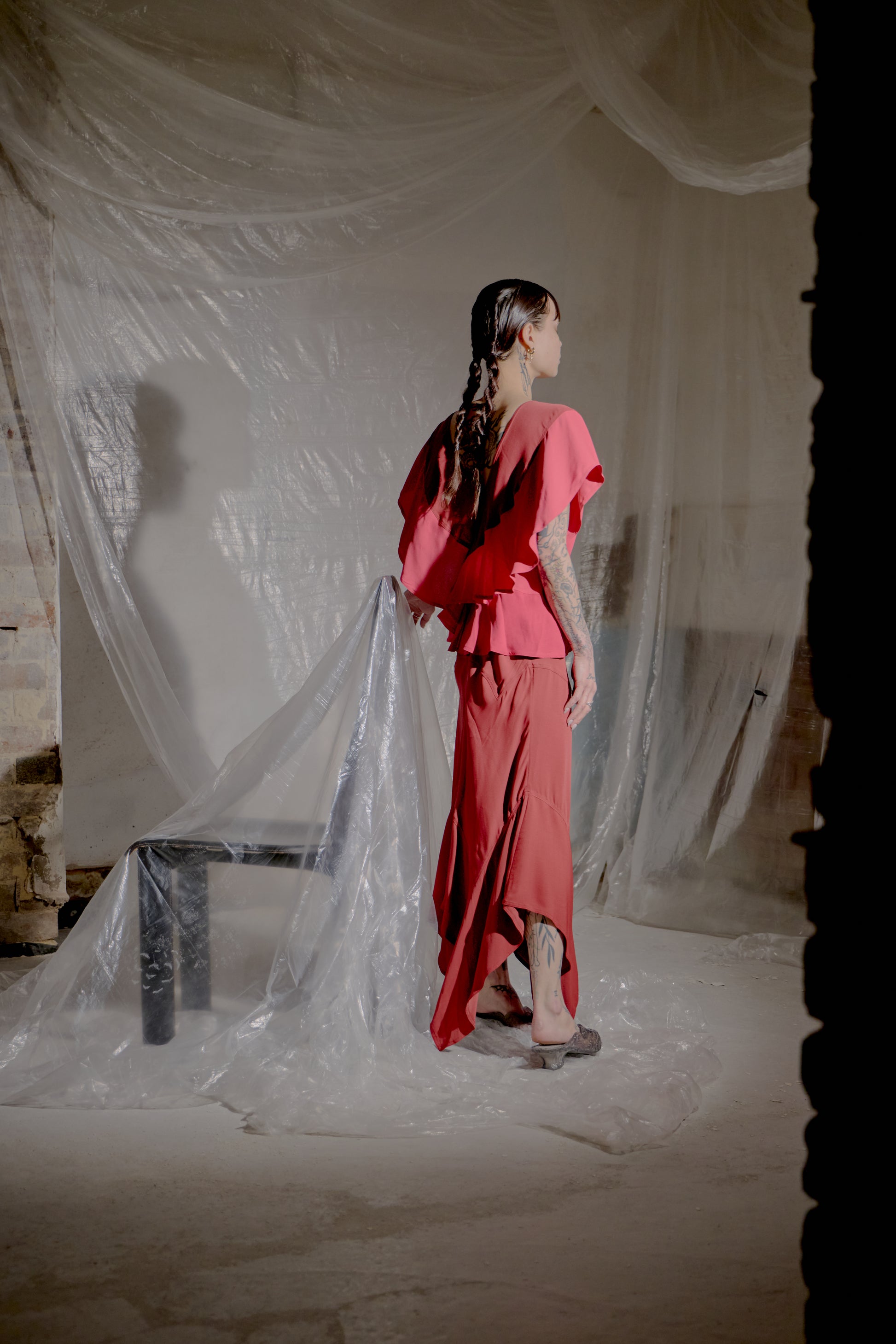 Woman in a red Saint Laurent outfit standing in a room with white plastic sheeting.